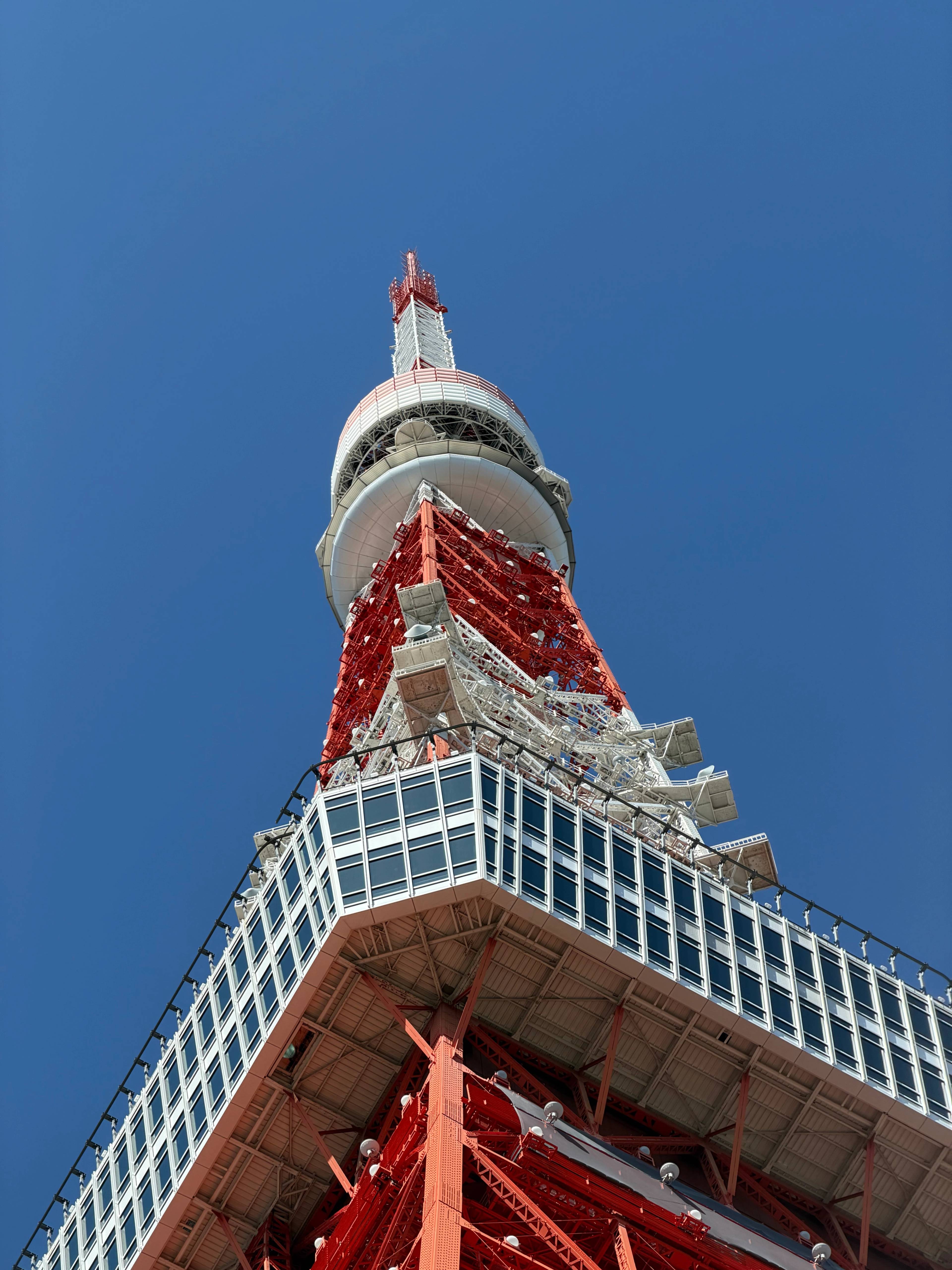 Tokyo Tower widziana z dołu na tle bezchmurnego nieba w Tokio, z charakterystyczną czerwono-białą konstrukcją.