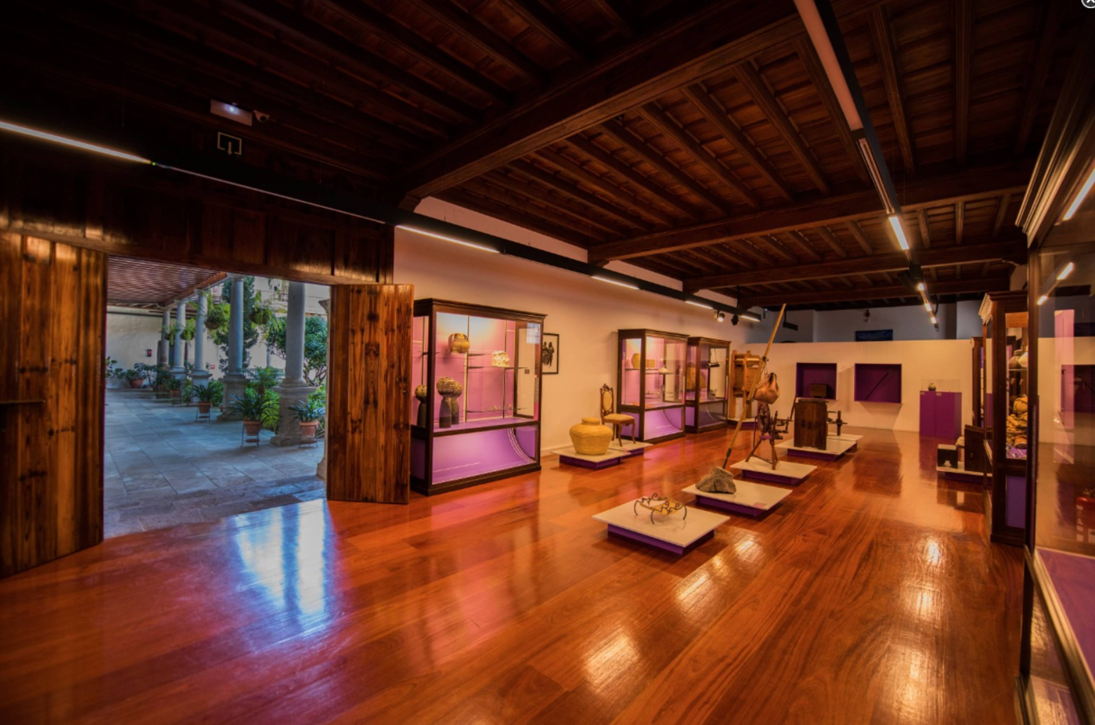 Wnętrze muzeum rzemiosła w La Orotava z drewnianą podłogą, przeszklonymi gablotami i eksponatami związanymi z kulturą Wysp Kanaryjskich.