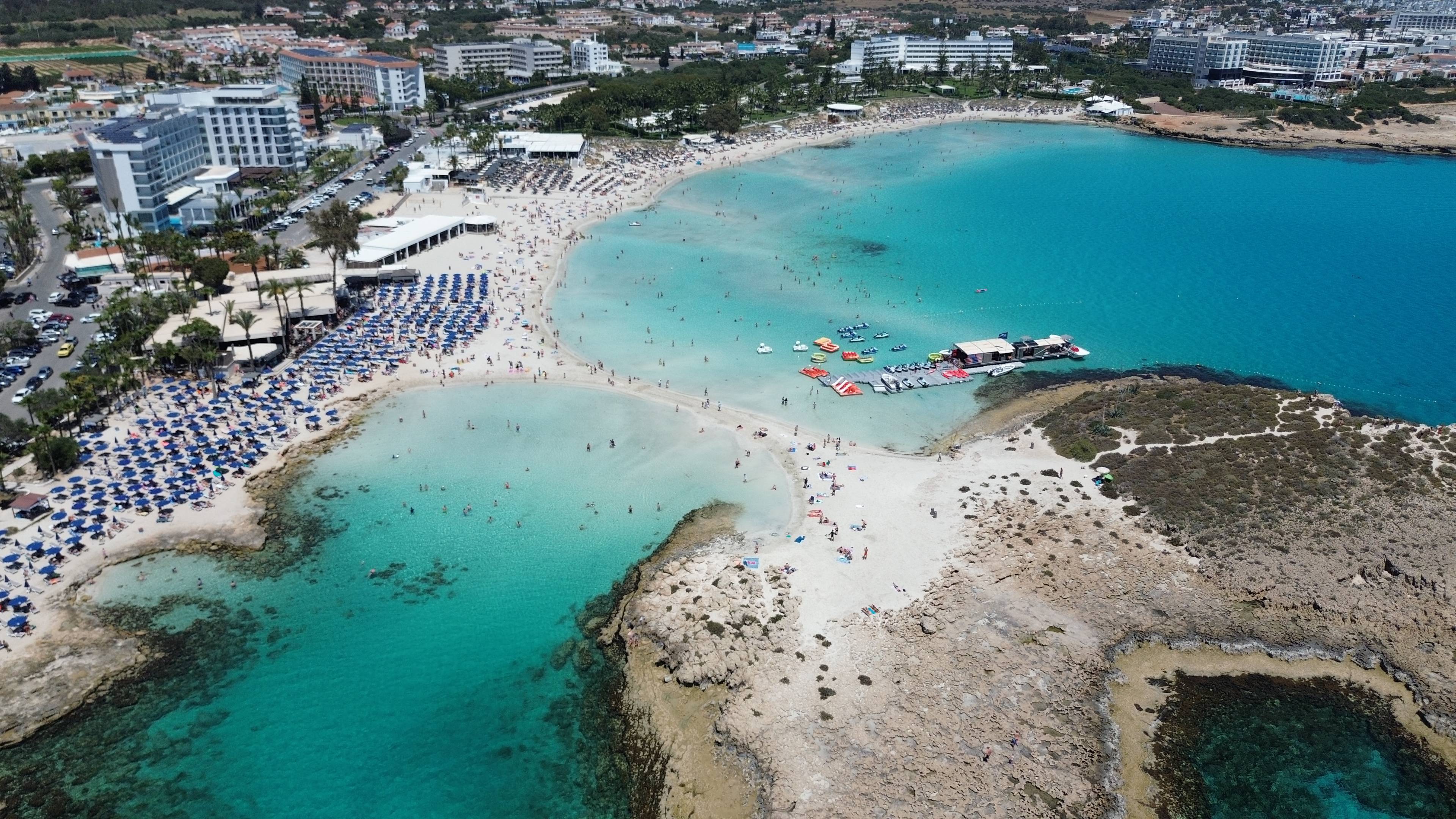 Panorama plaży Nissi Beach w Ayia Napa na Cyprze z jasnym piaskiem, turkusową wodą i strefą leżaków.