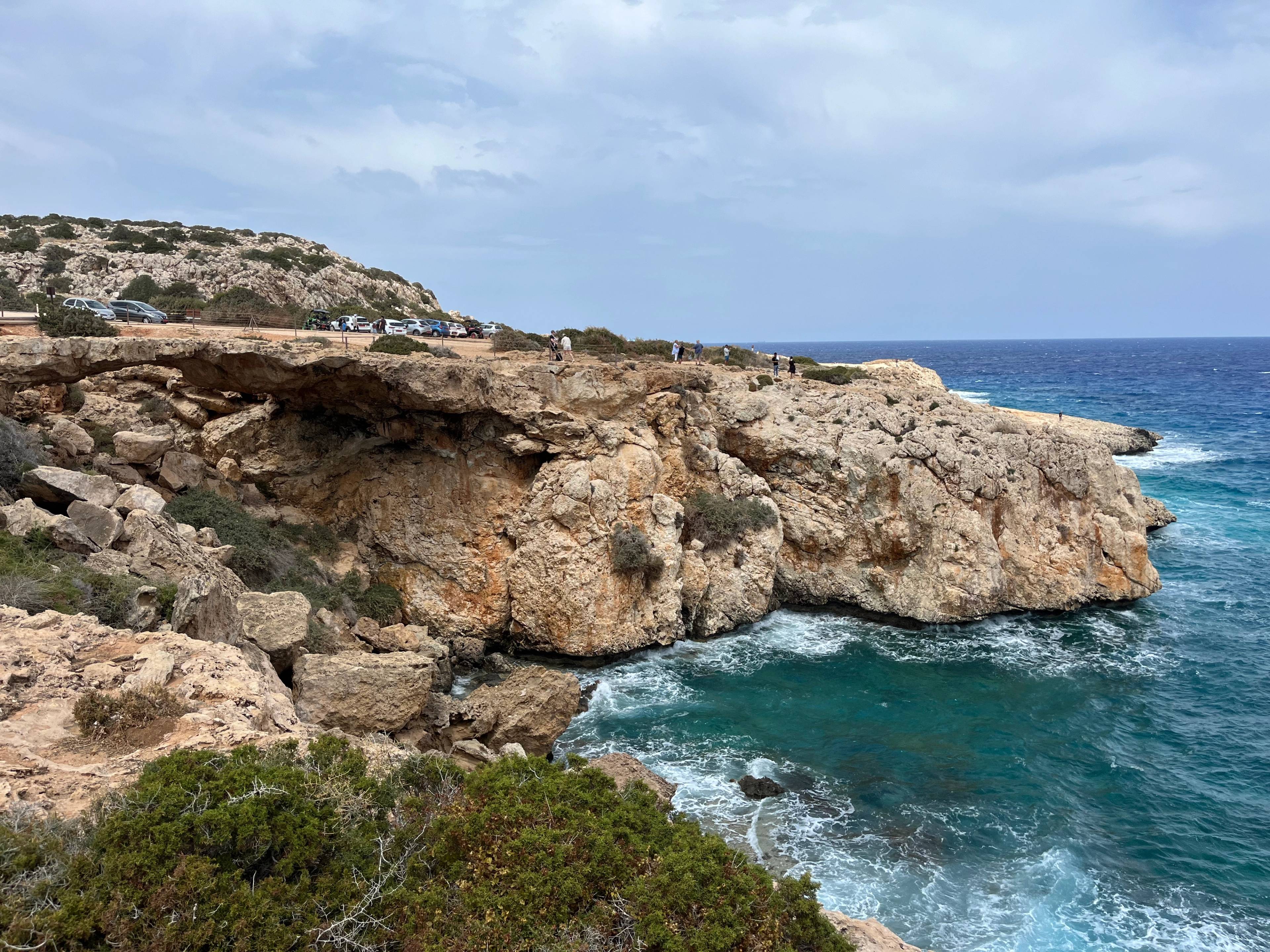 Skaliste klify nad turkusowym morzem w Cape Greco na Cyprze, z falami rozbijającymi się o skały.
