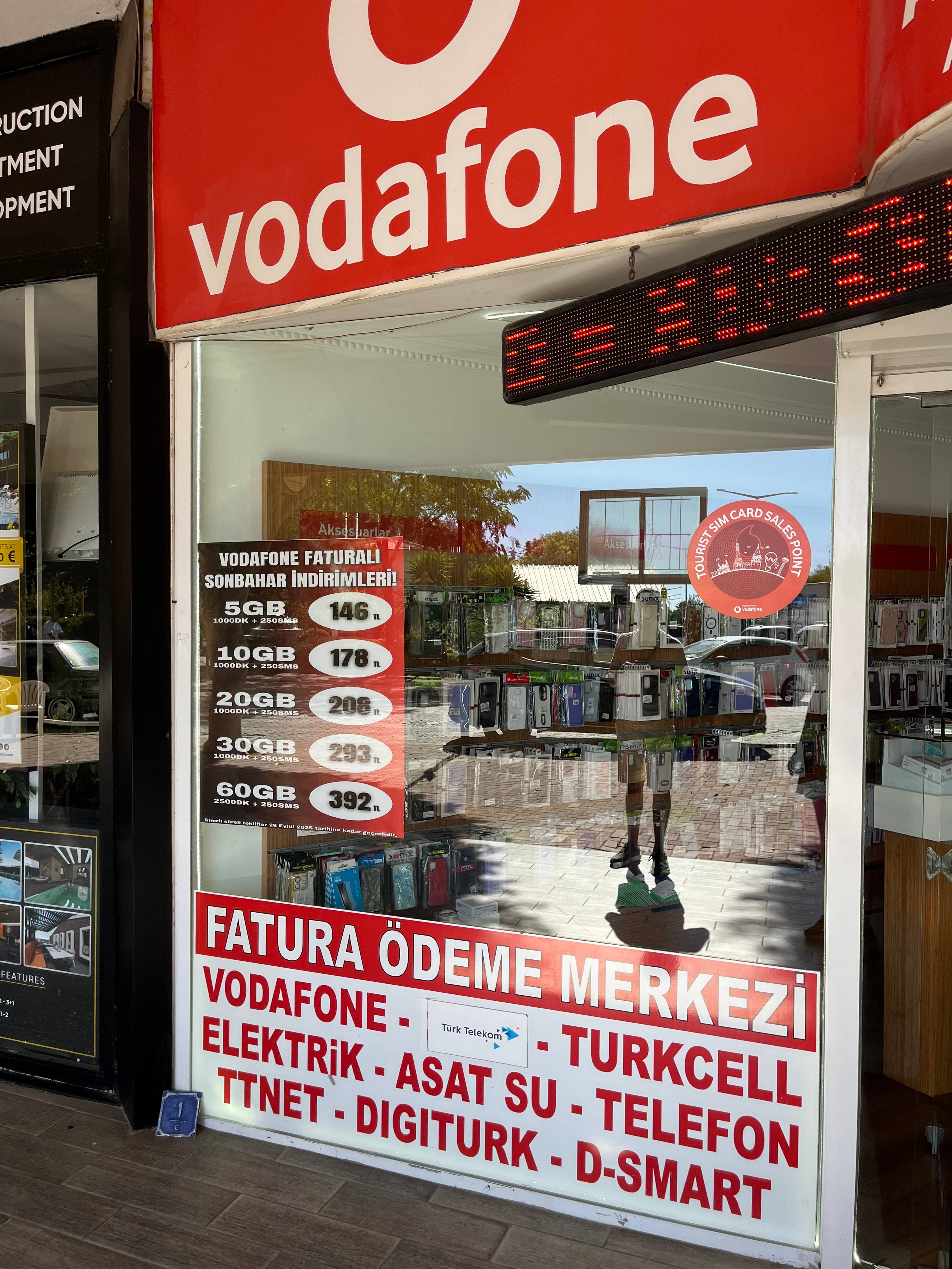 Wejście do punktu Vodafone z czerwonym szyldem i tablicą usług w języku tureckim.