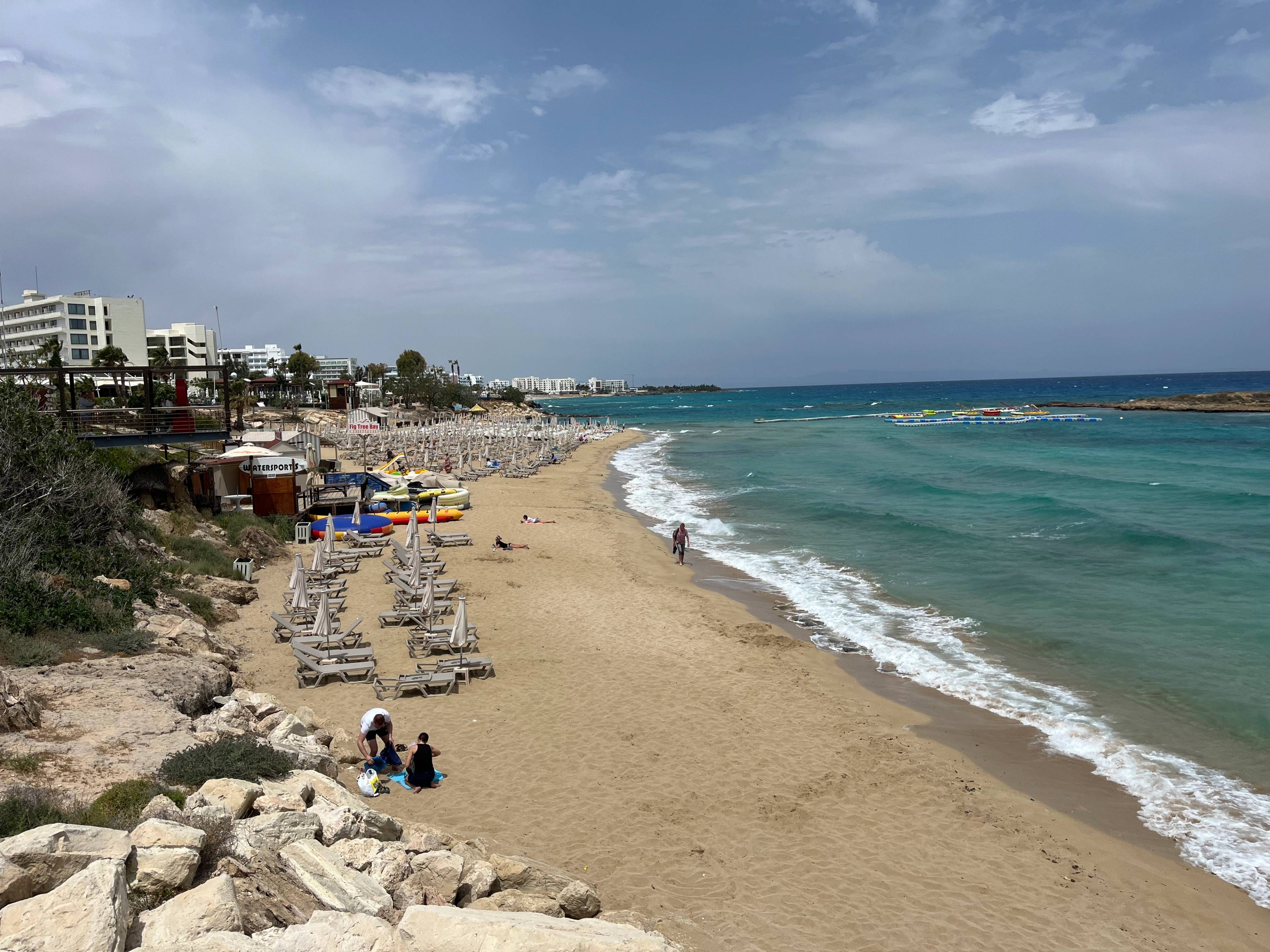 Piaszczysta plaża w Protaras na Cyprze z rzędem leżaków, turkusowym morzem i hotelami w tle.