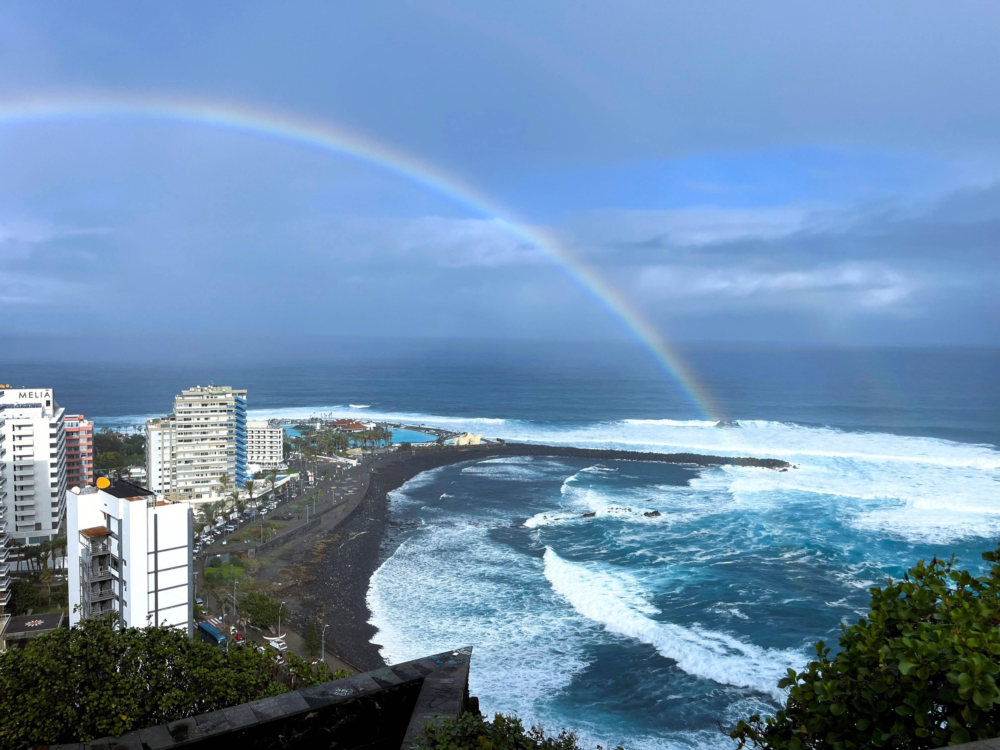 Panorama oceanu z tęczą nad falami i skalistym wybrzeżem.