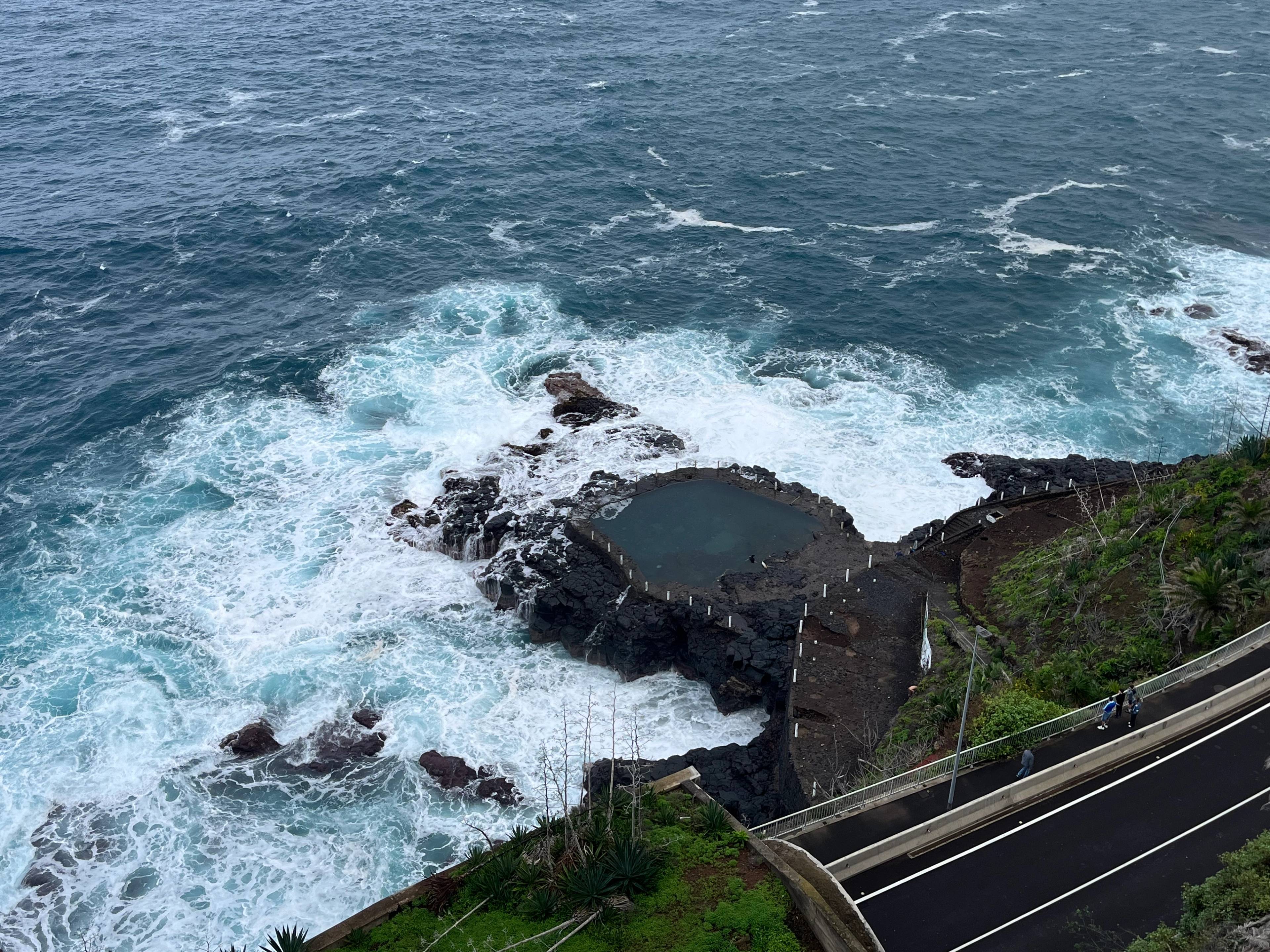 Skaliste wybrzeże z falami oceanu rozbijającymi się o czarne skały i naturalnie uformowany basen w skałach. 