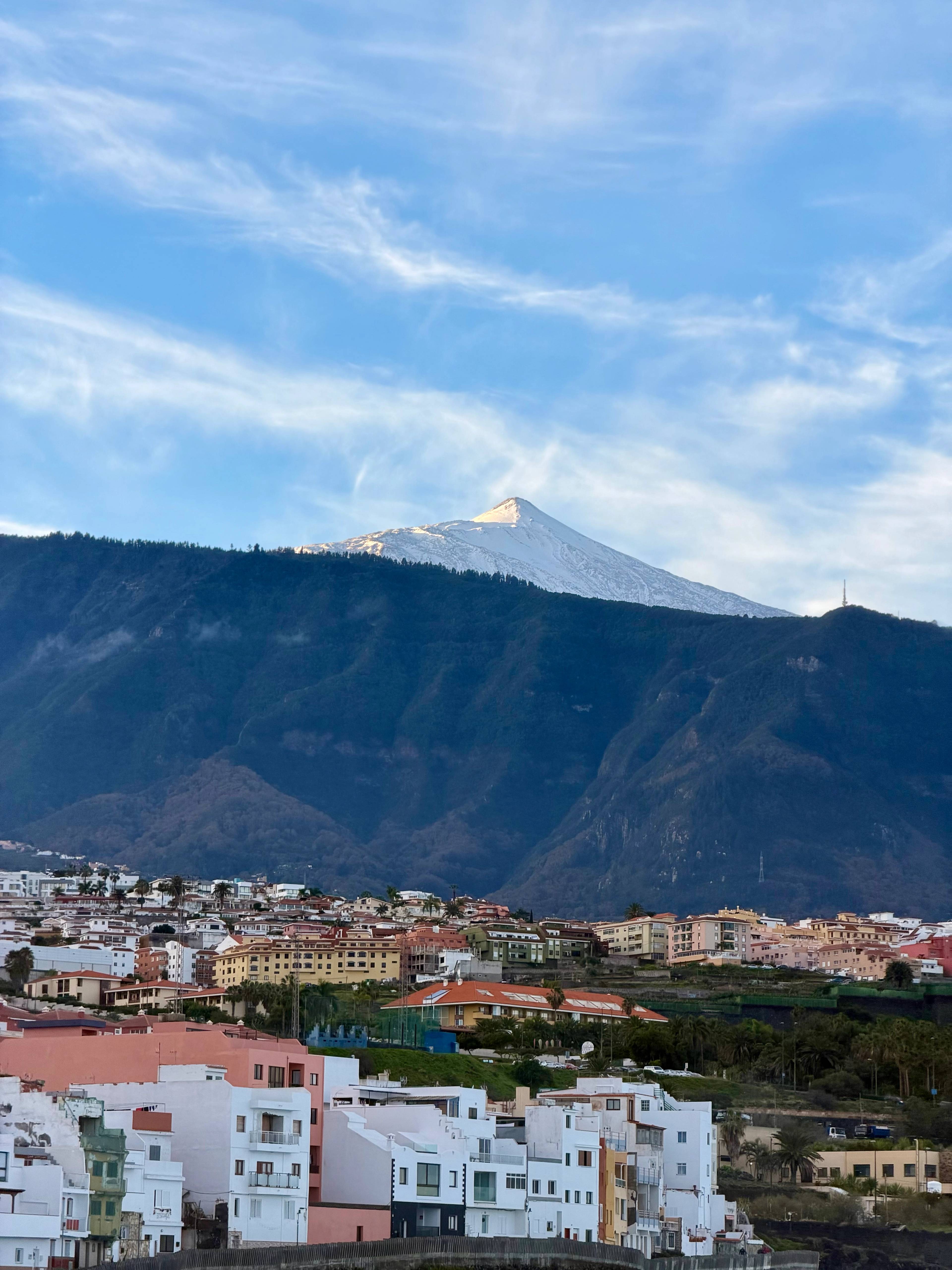 Panorama miasta z białymi budynkami i wulkanem w tle pod błękitnym niebem.