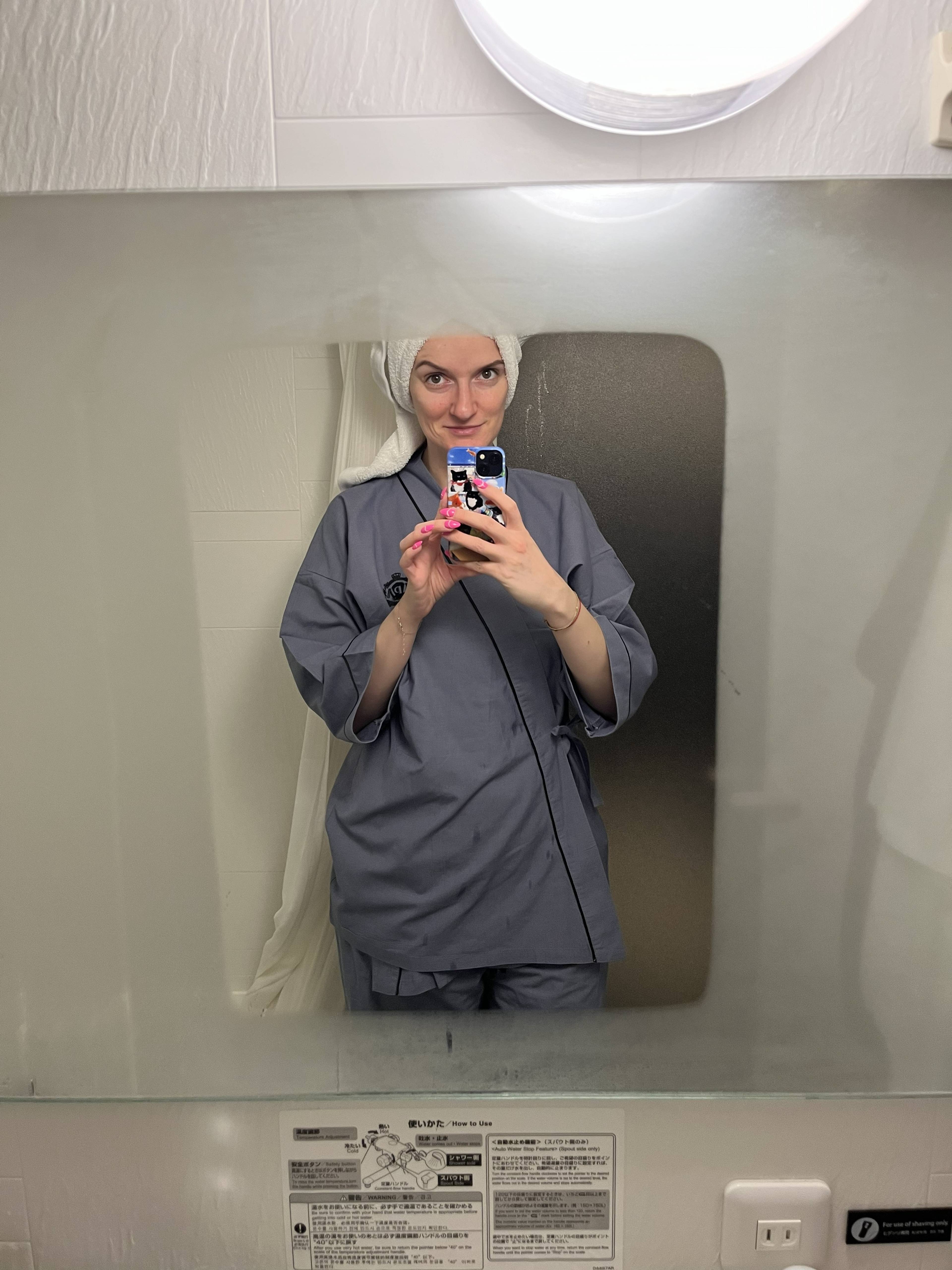 Kobieta w ręczniku na głowie i japońskiej piżamie przed lustrem w hotelowej łazience.