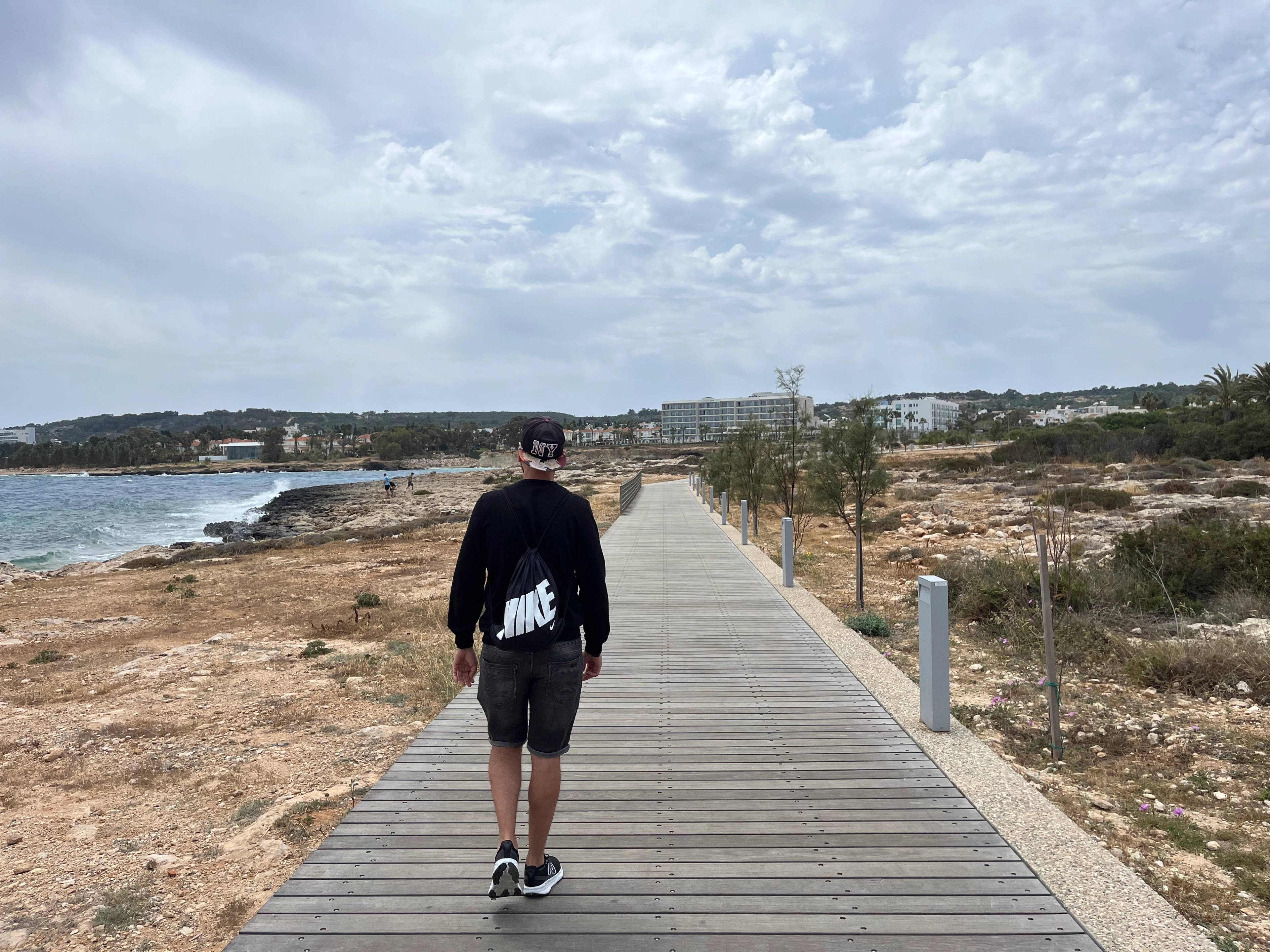 Drewniany pomost - promenada prowadzący przez stepowy krajobraz nad morzem. Na pierwszym planie widok na mężczyznę idącego przed siebie.