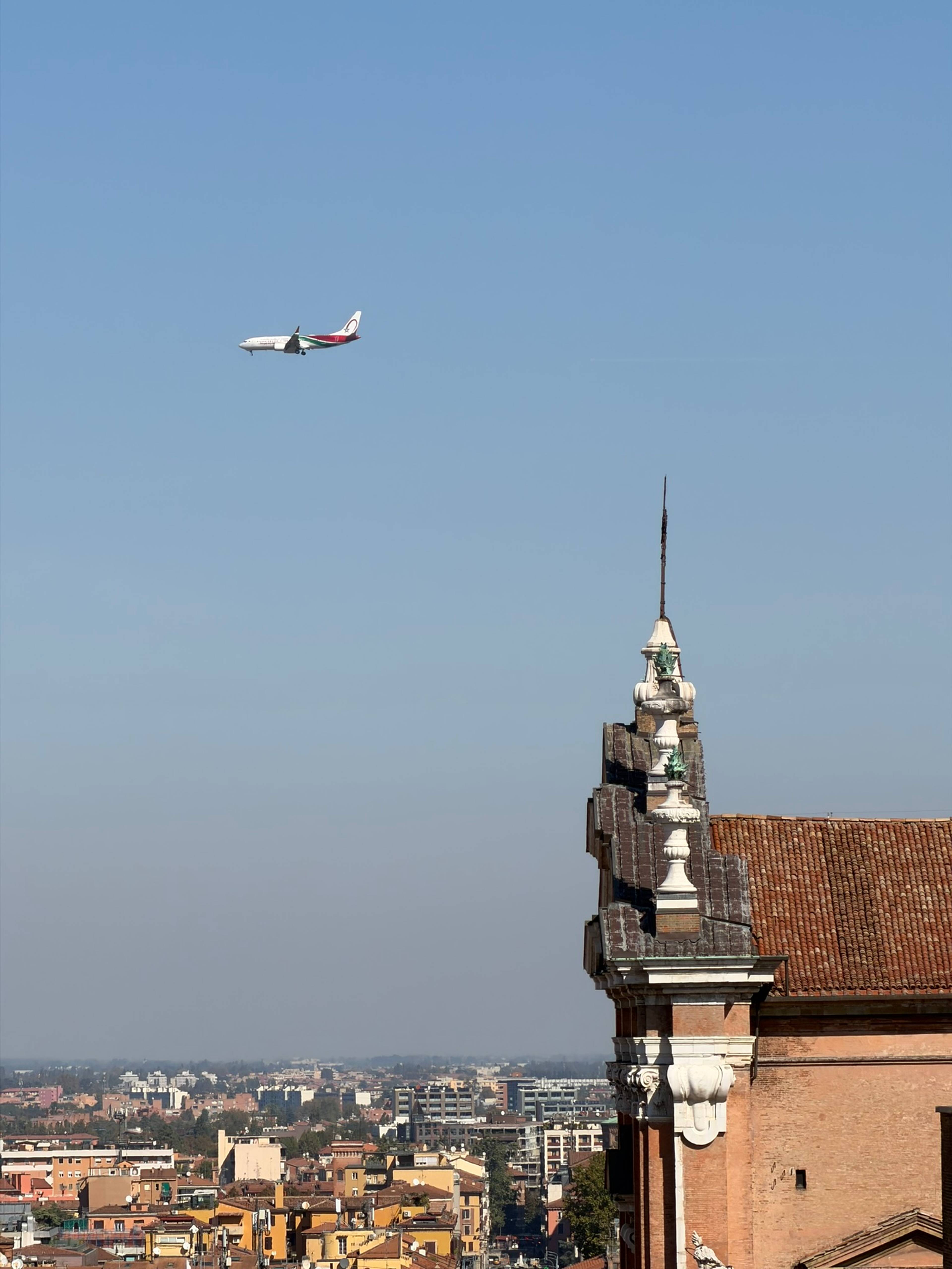 Samolot pasażerski przelatuje na błękitnym niebie nad ceglanym budynkiem.