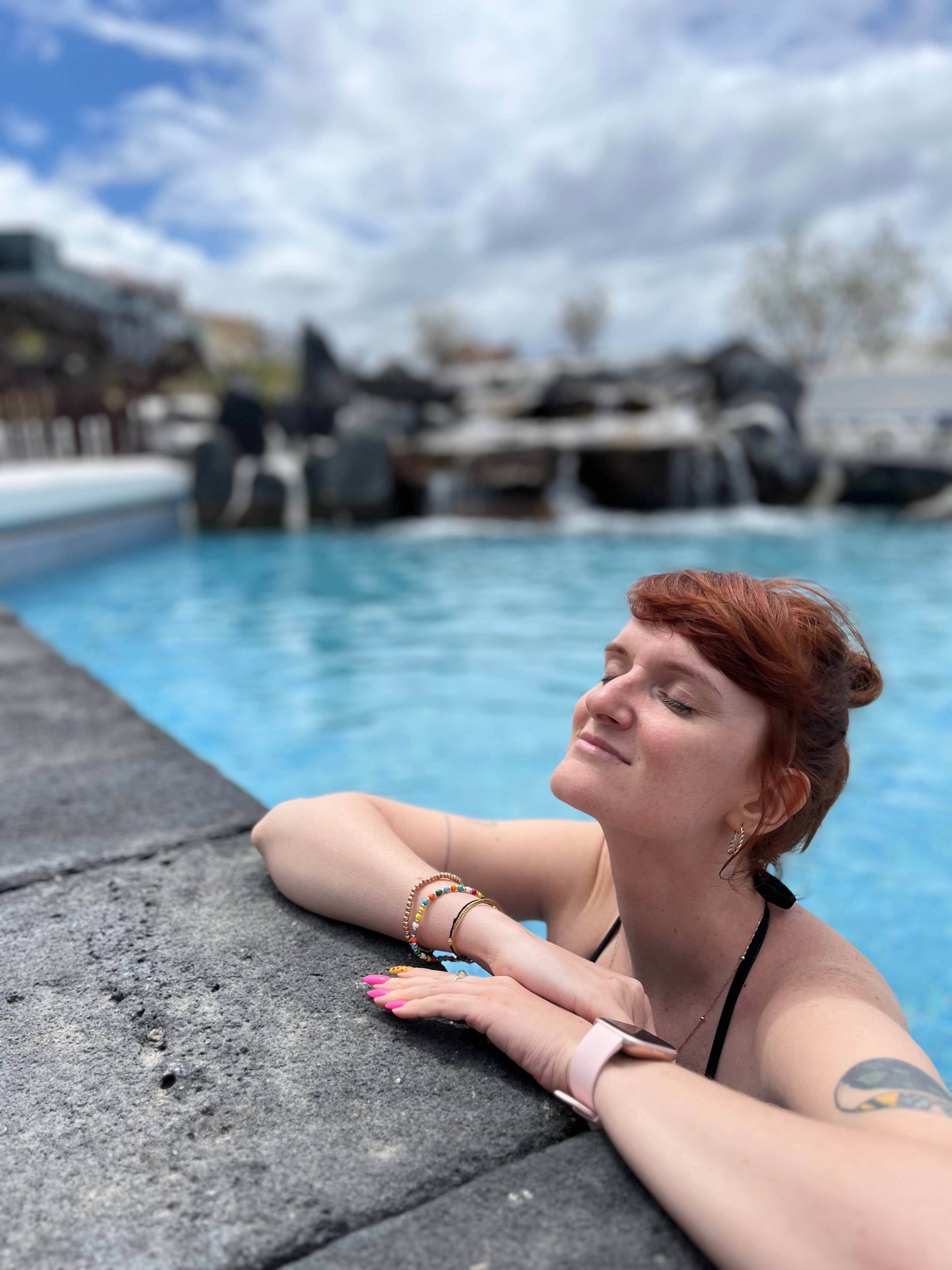 Kobieta opiera się o krawędź basenu z widokiem na ocean.