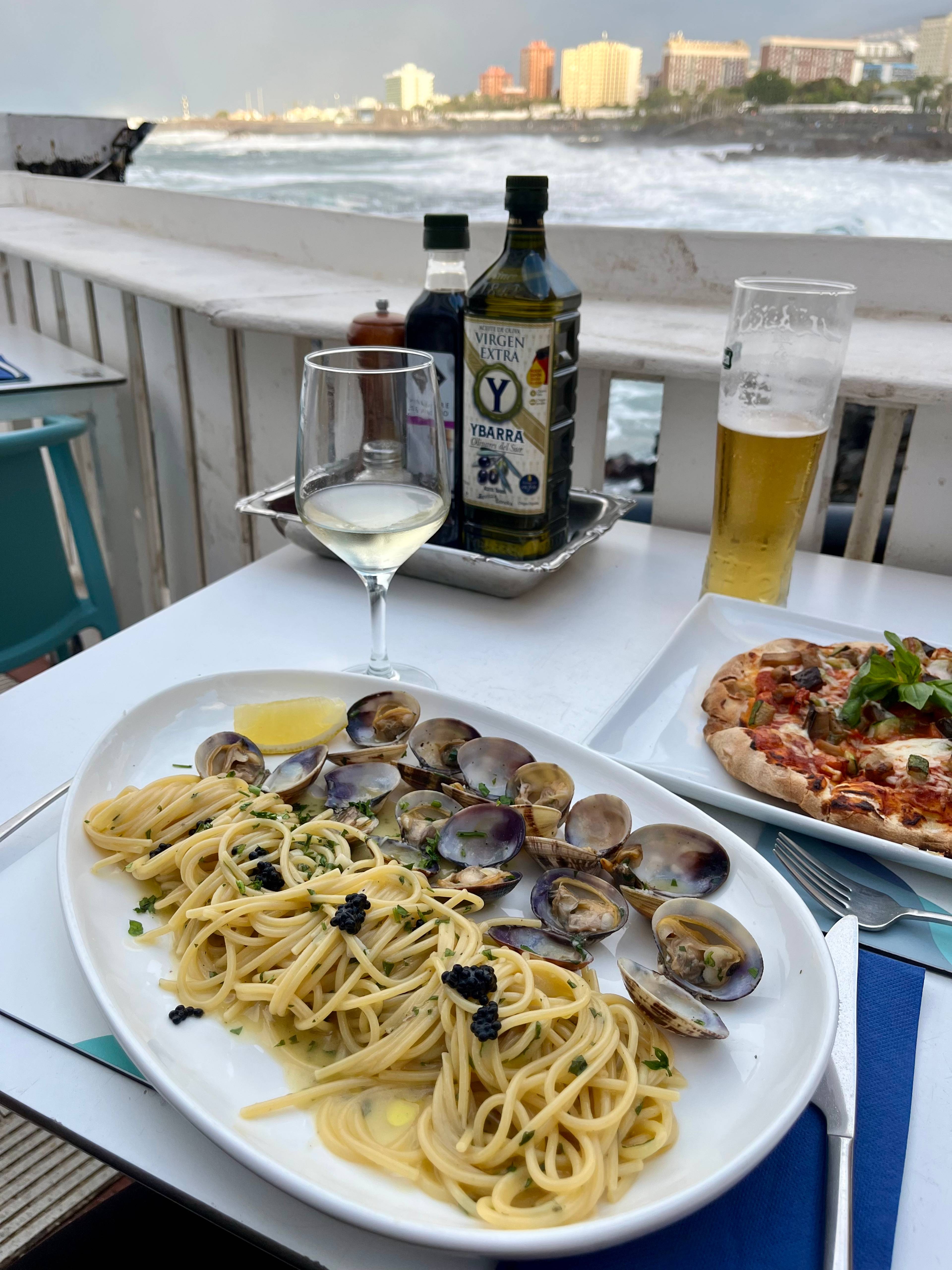 Stół z talerzem makaronu, owocami morza, pieczywem i butelkami oliwy.