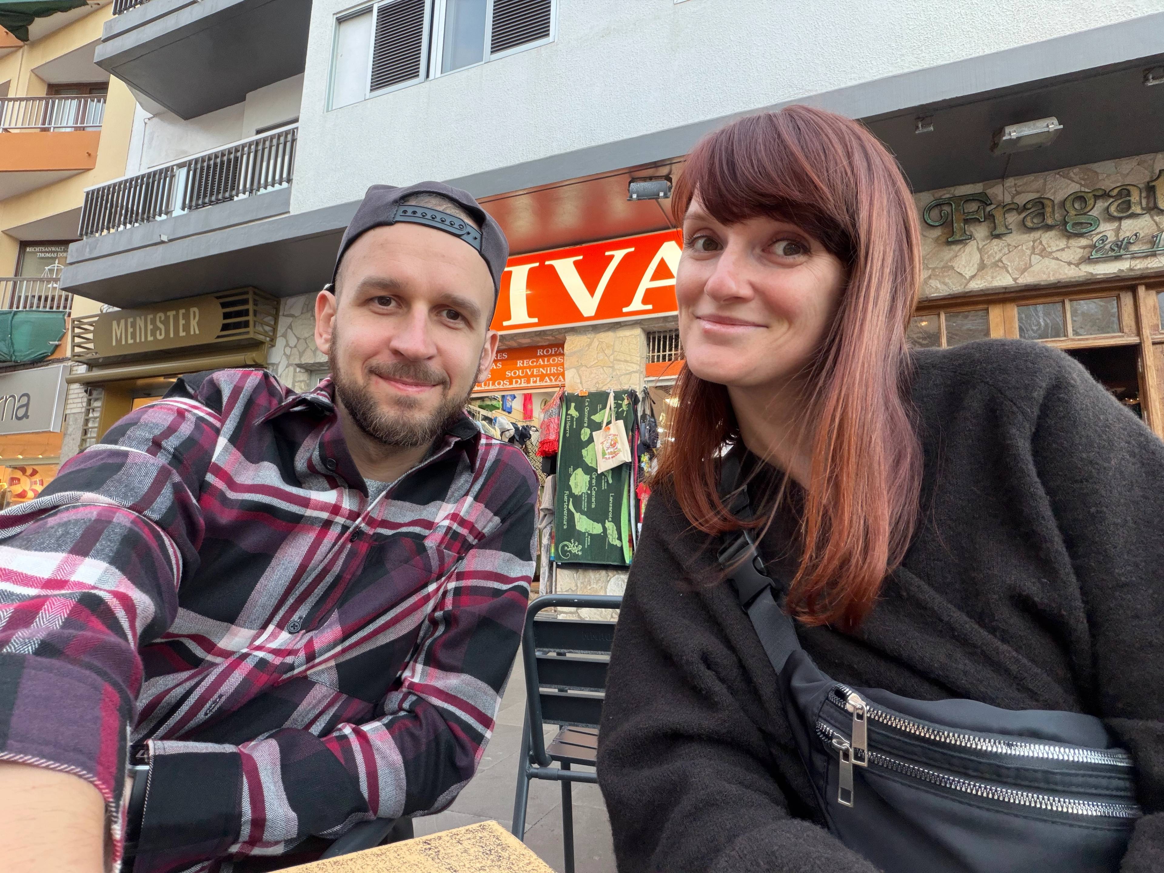 Dwie osoby siedzące w ogródku restauracyjnym na dworze przed kamienicą.