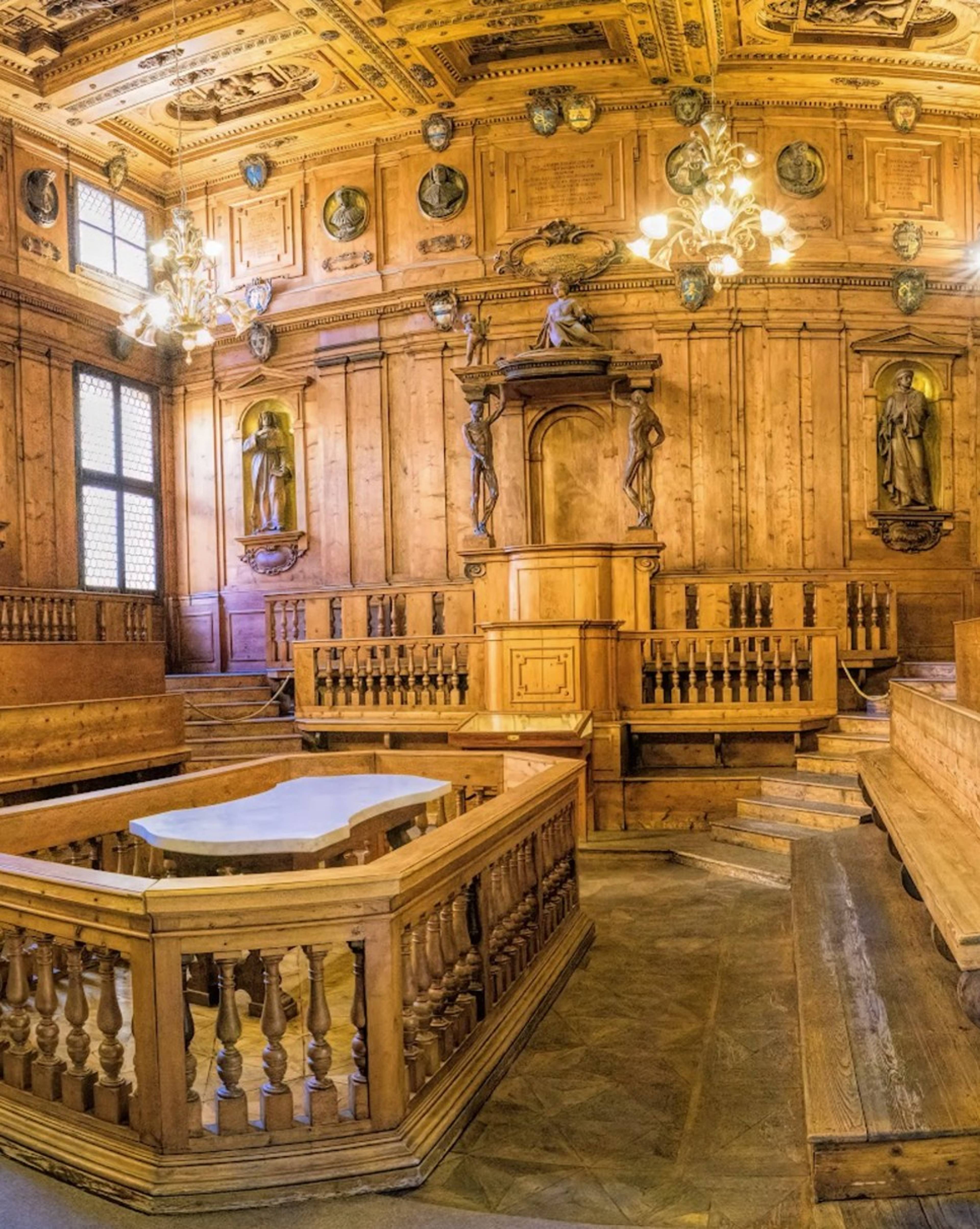 Zabytkowe drewniane wnętrze teatru anatomicznego z centralnym stołem, ławami, rzeźbami i ozdobnym sufitem.