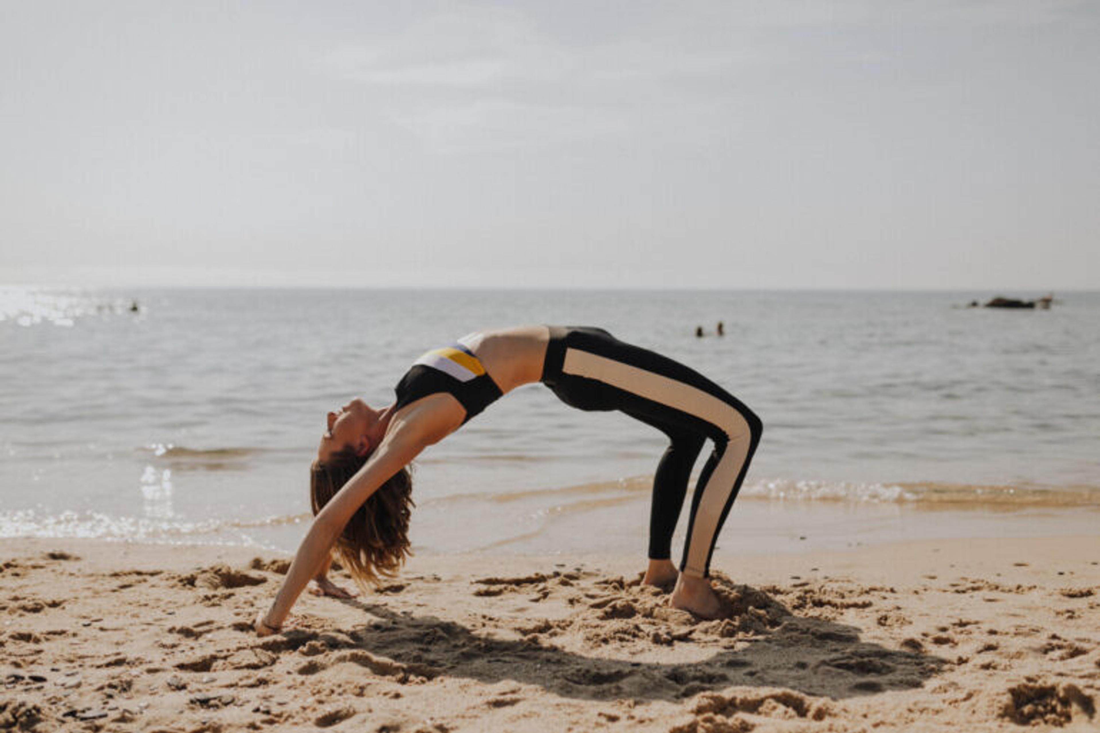 Dziewczyna w stroju sportowym robi ćwiczenie - myostek na plaży, w tle morze