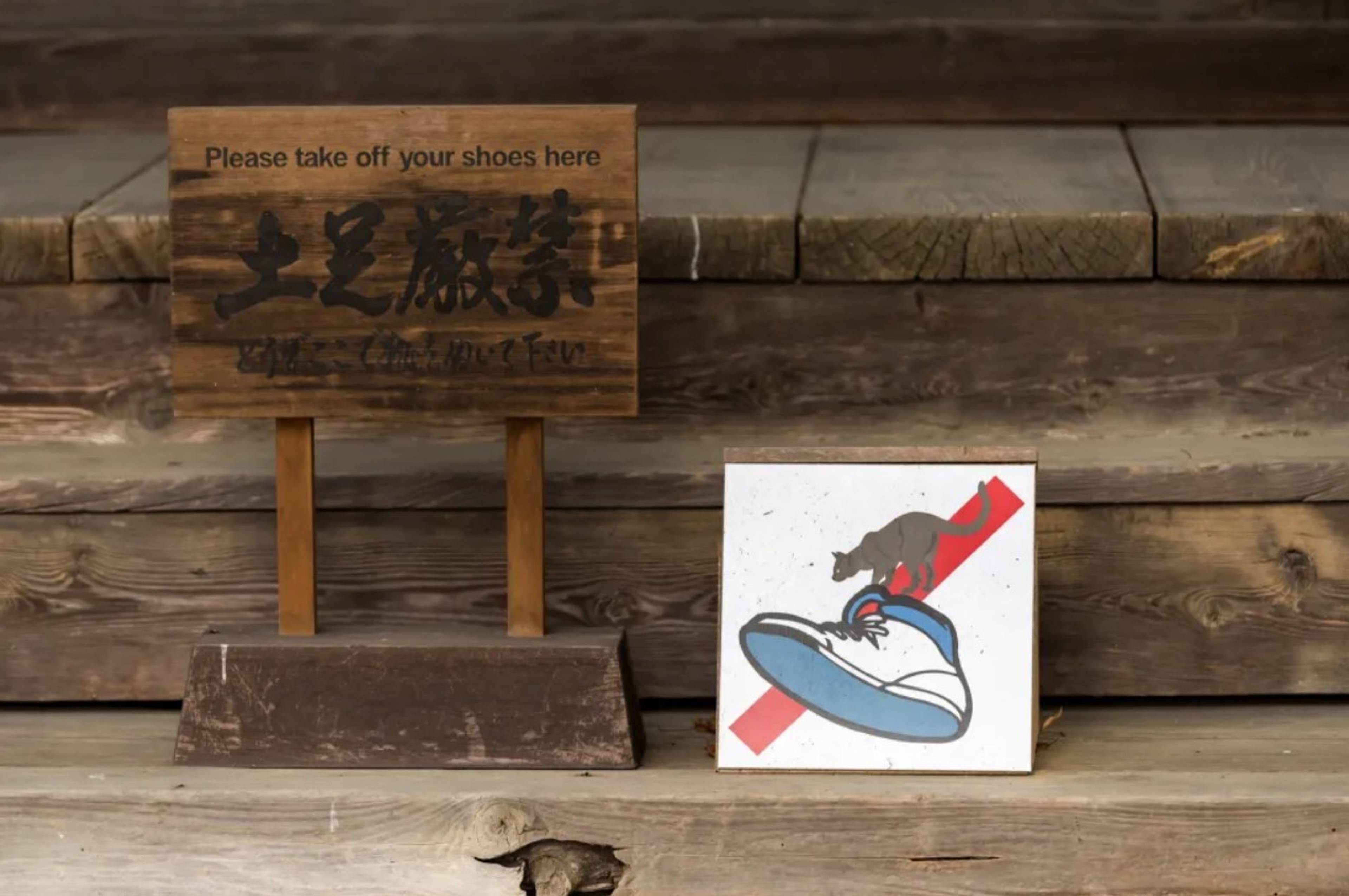 Drewniane schody z tabliczką informującą „Please take off your shoes here” oraz znakiem graficznym zakazu wchodzenia w butach.