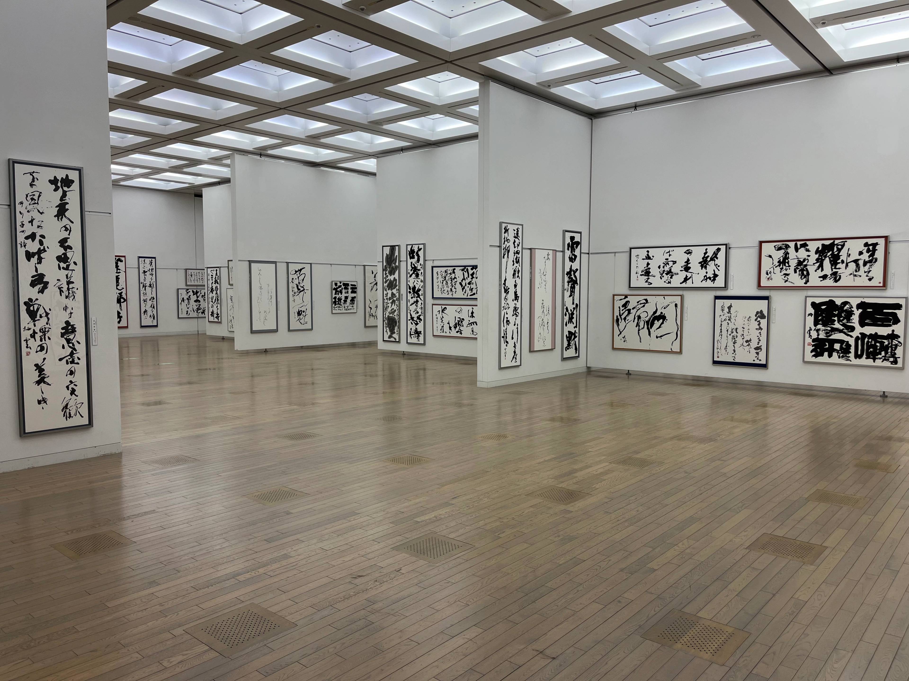 Wnętrze galerii sztuki w Japonii z wystawą kaligrafii na ścianach i drewnianą podłogą.