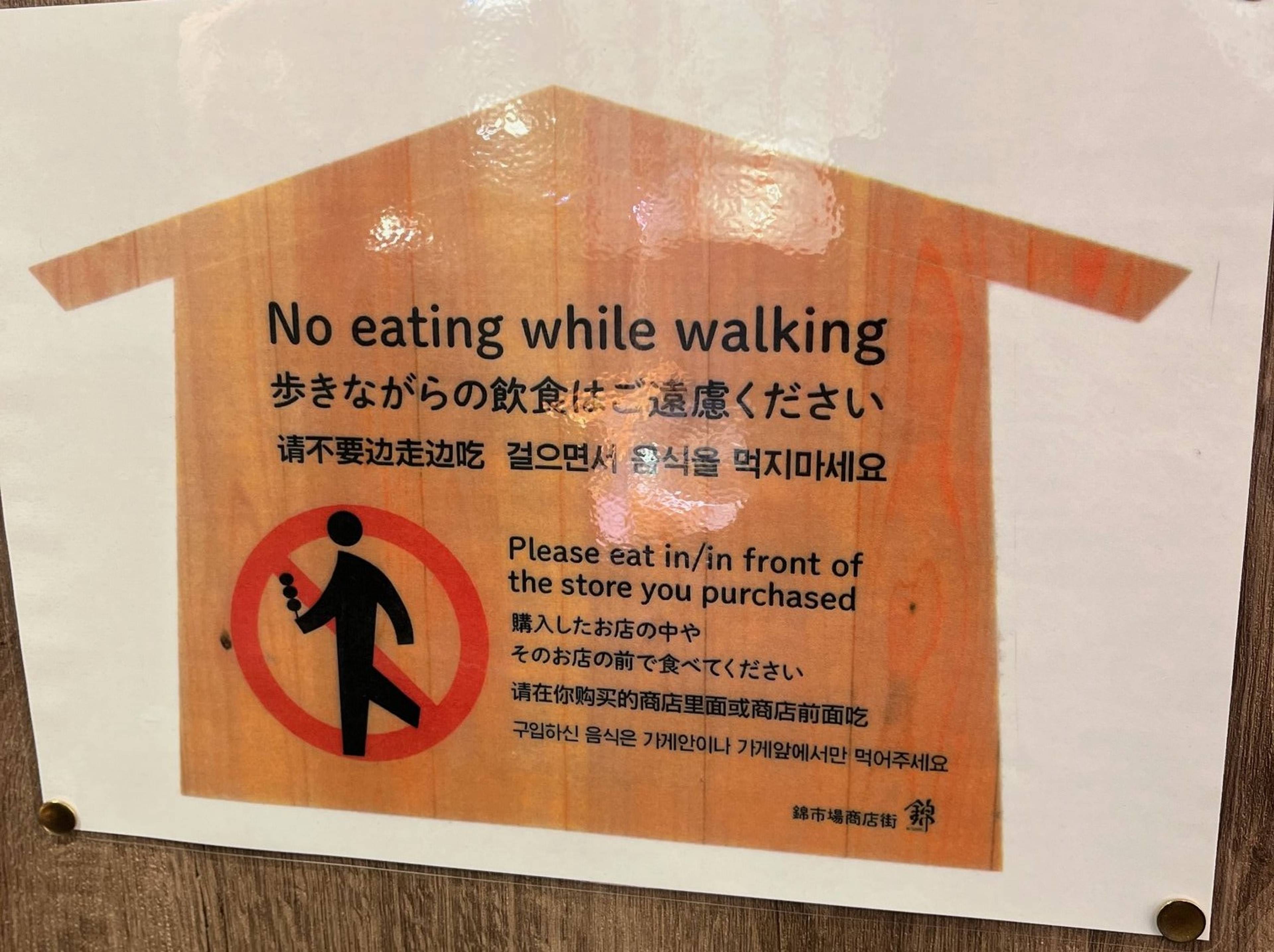 Znak informacyjny z piktogramem zakazu i napisem „No eating while walking”, informujący, aby nie jeść podczas chodzenia.