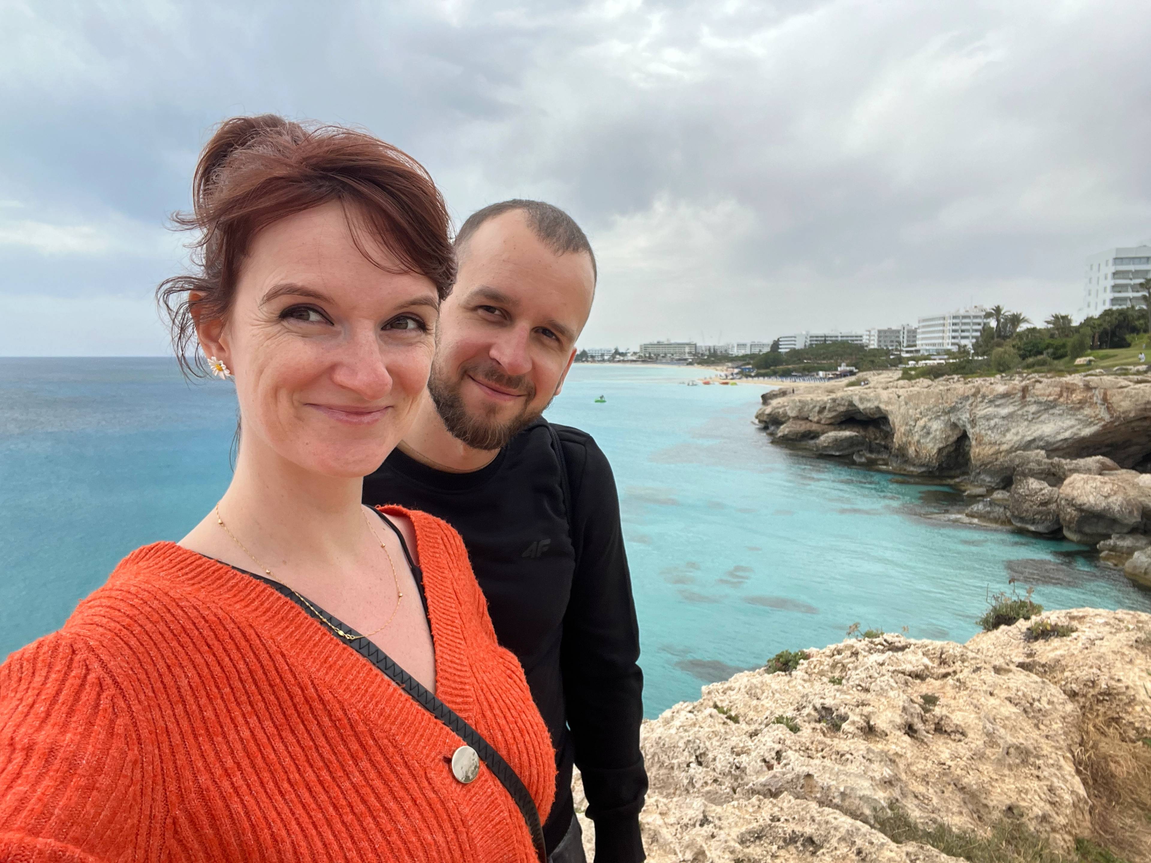 Uśmiechnięta para na tle morskiej wody i jaskiń w klifie.