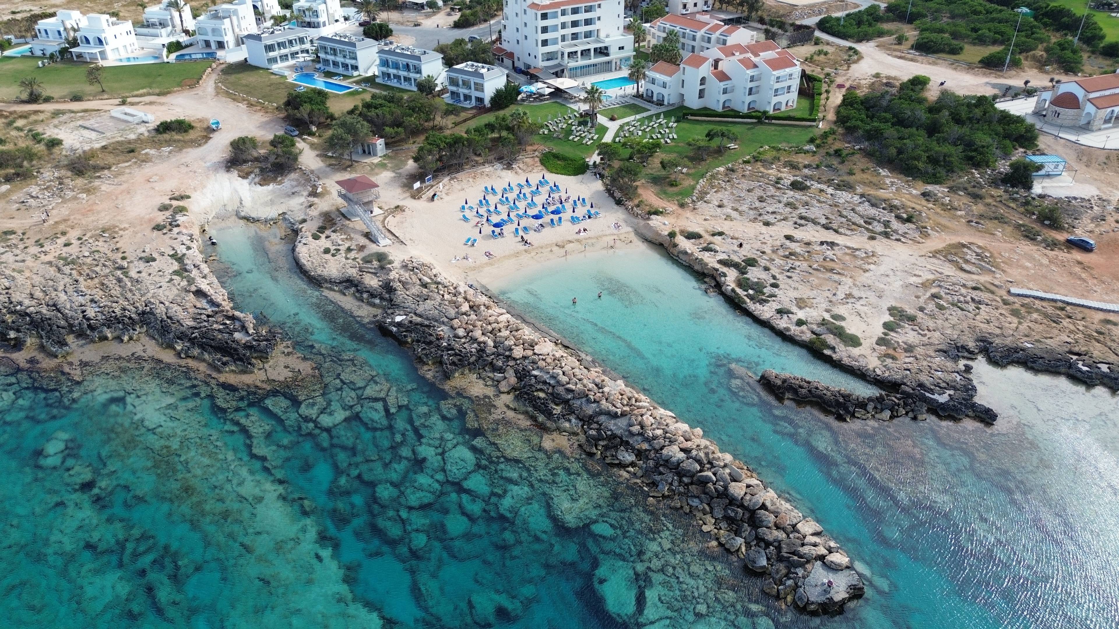 Widok z lotu ptaka na zatokę z kamiennym falochronem i turkusową wodą w Protaras na Cyprze.