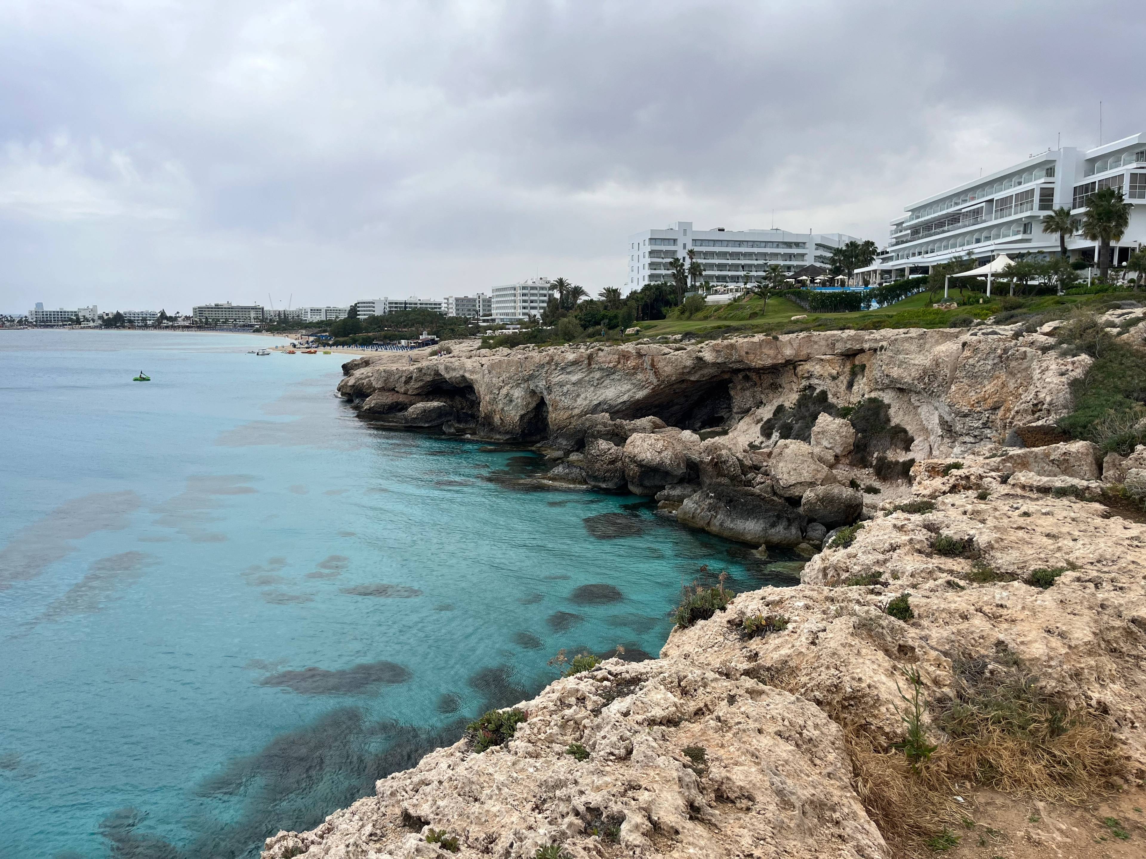 Klifowe wybrzeże Ayia Napa na Cyprze z turkusowym morzem i widocznymi hotelami w tle.