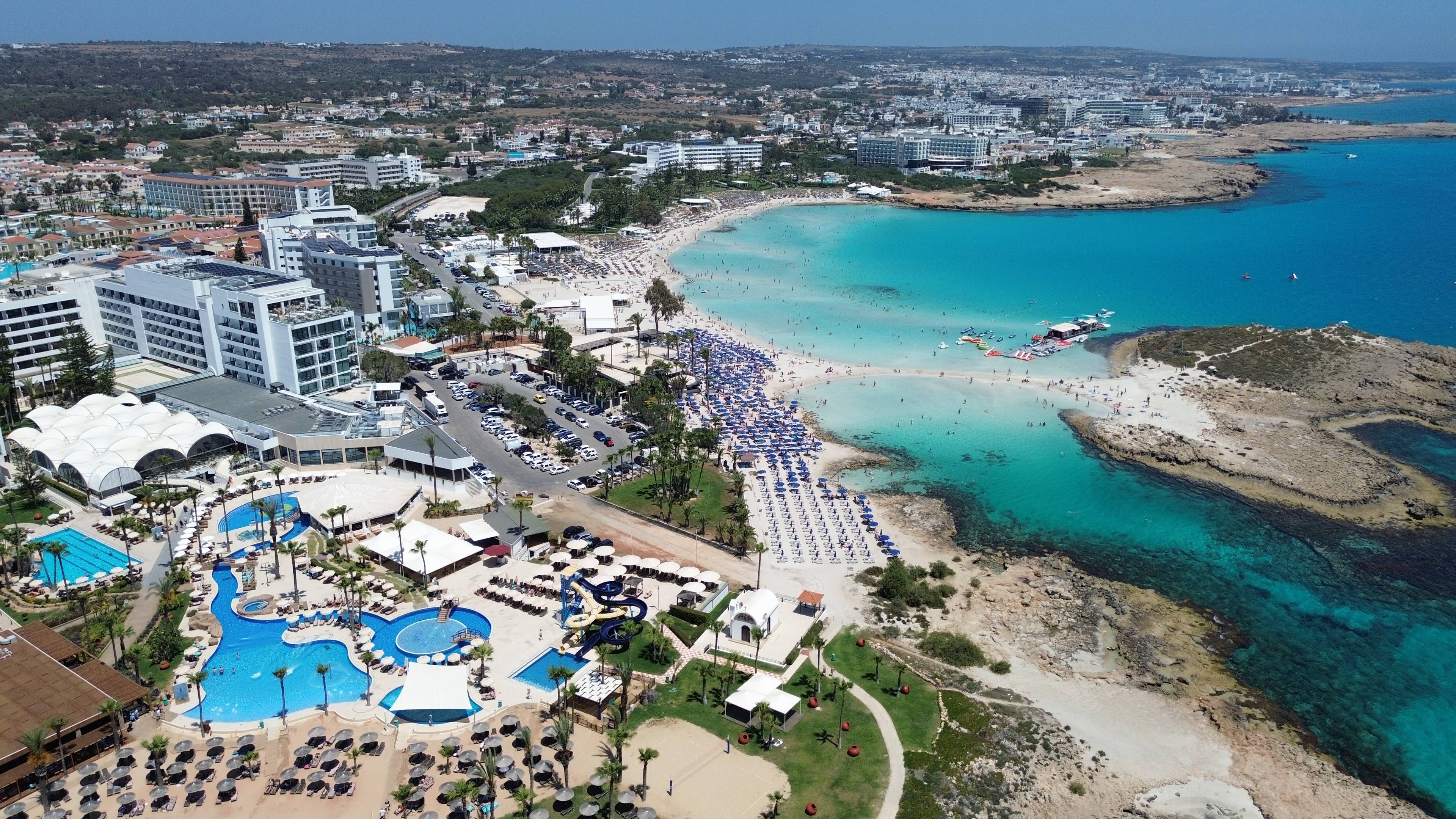Widok z lotu ptaka na kompleks hotelowy i plażę Nissi Beach w Ayia Napa na Cyprze, otoczoną turkusowym morzem.