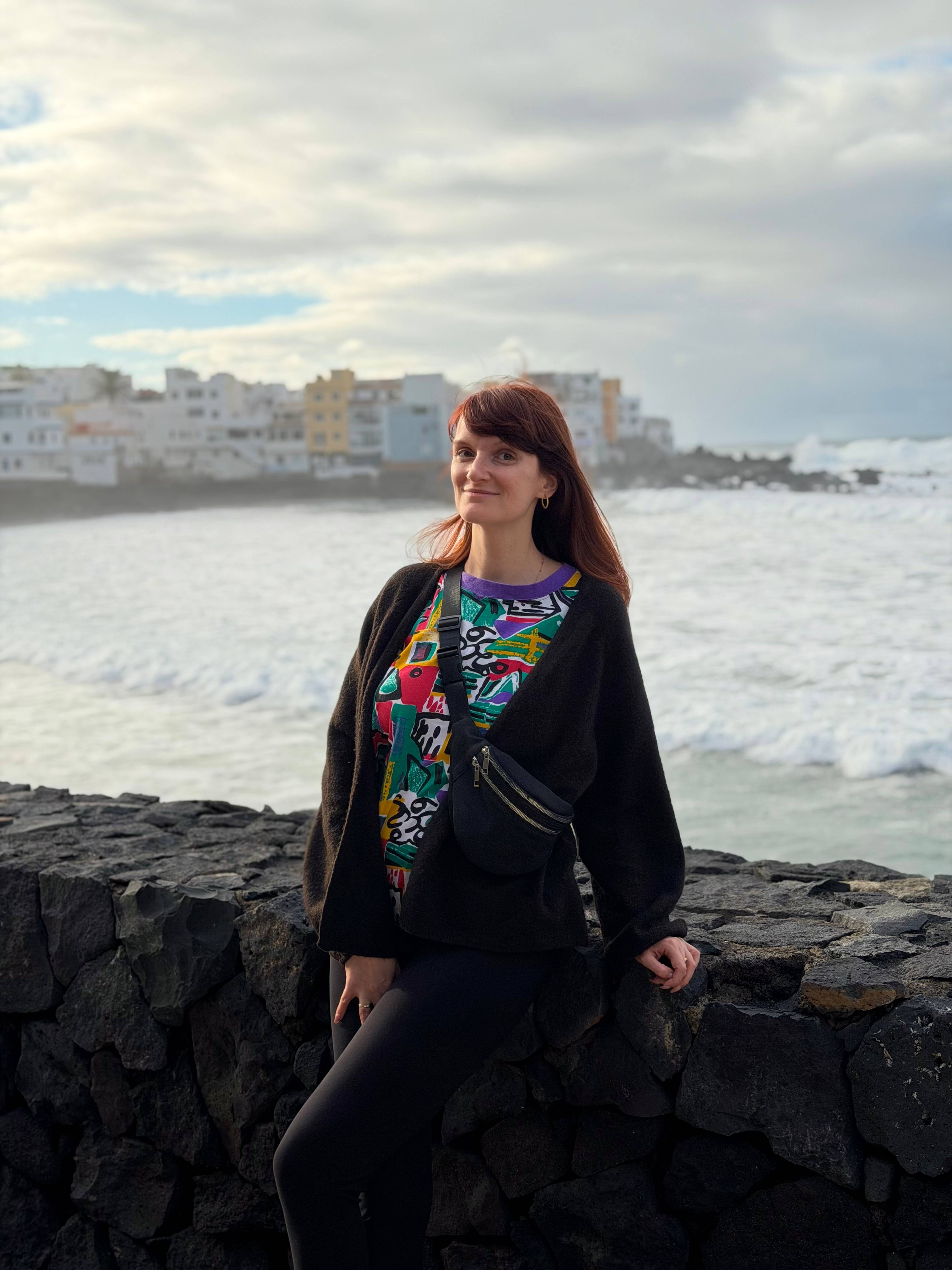 Kobieta stoi przy kamiennym murku z widokiem na ocean i zachmurzone niebo.