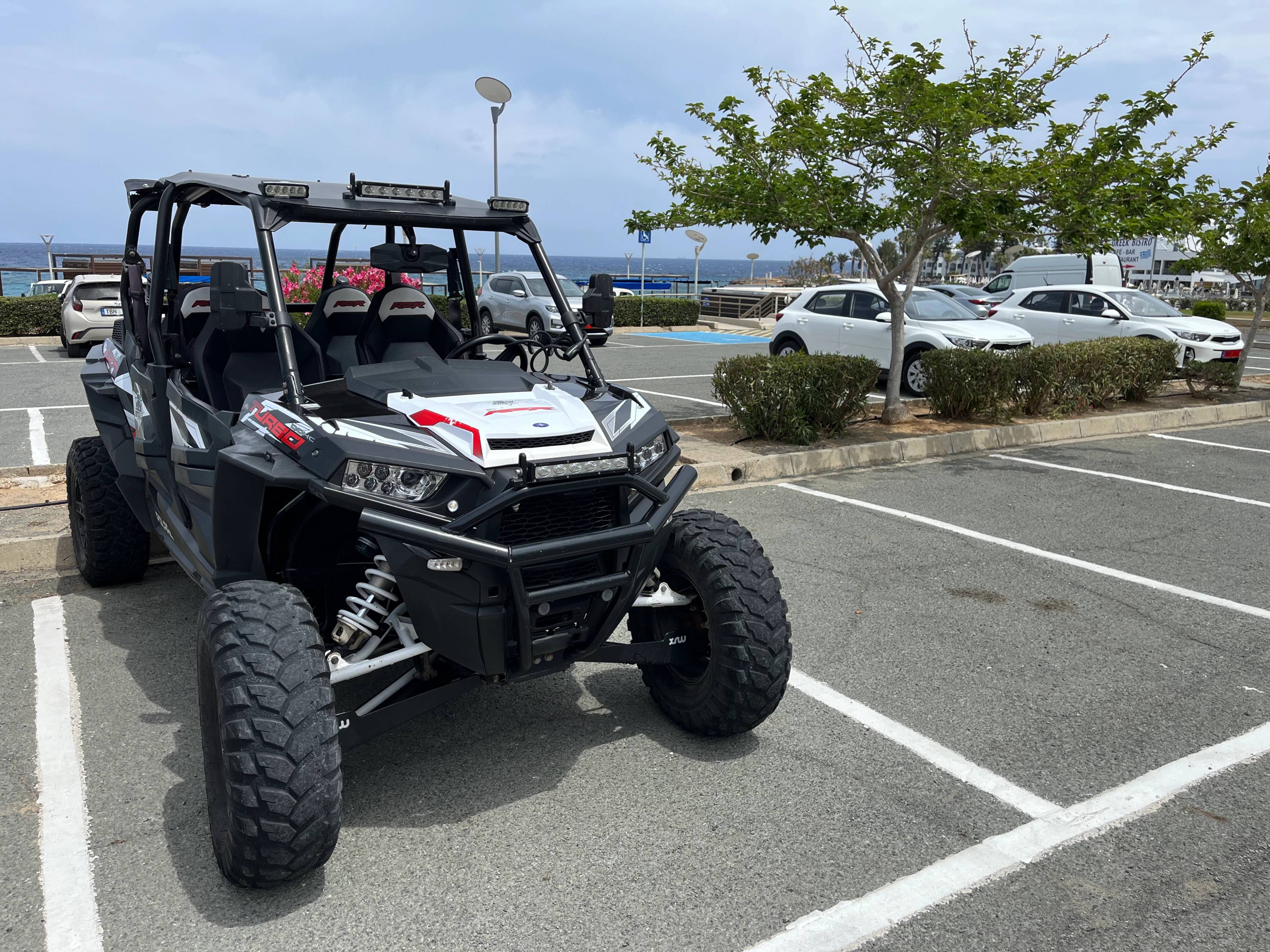 Pojazd terenowy typu buggy zaparkowany na parkingu w Protaras na Cyprze, z widokiem na morze w tle.