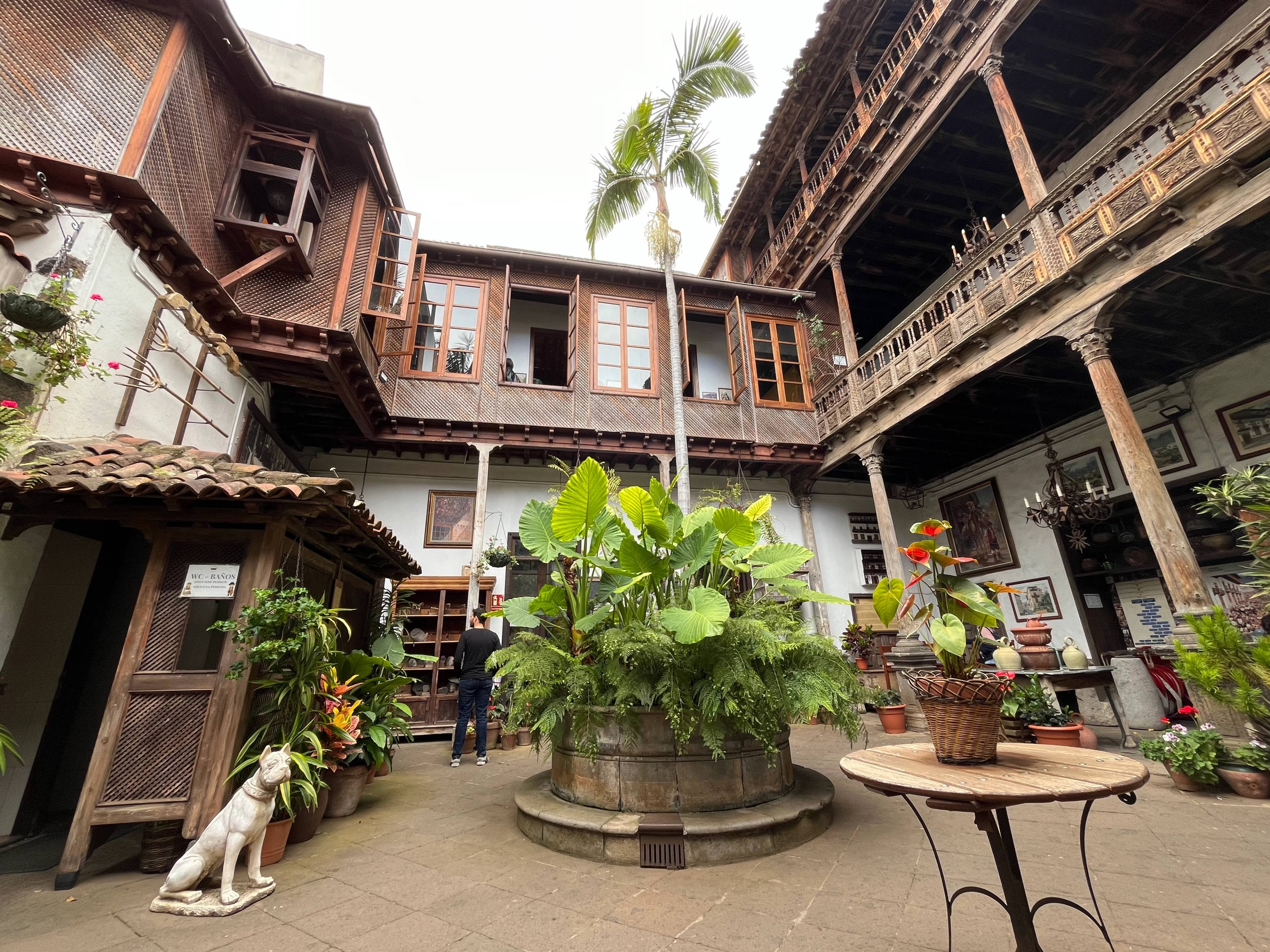 Dziedziniec Casa de los Balcones z drewnianymi balkonami i dużą donicą z tropikalnymi roślinami pośrodku.