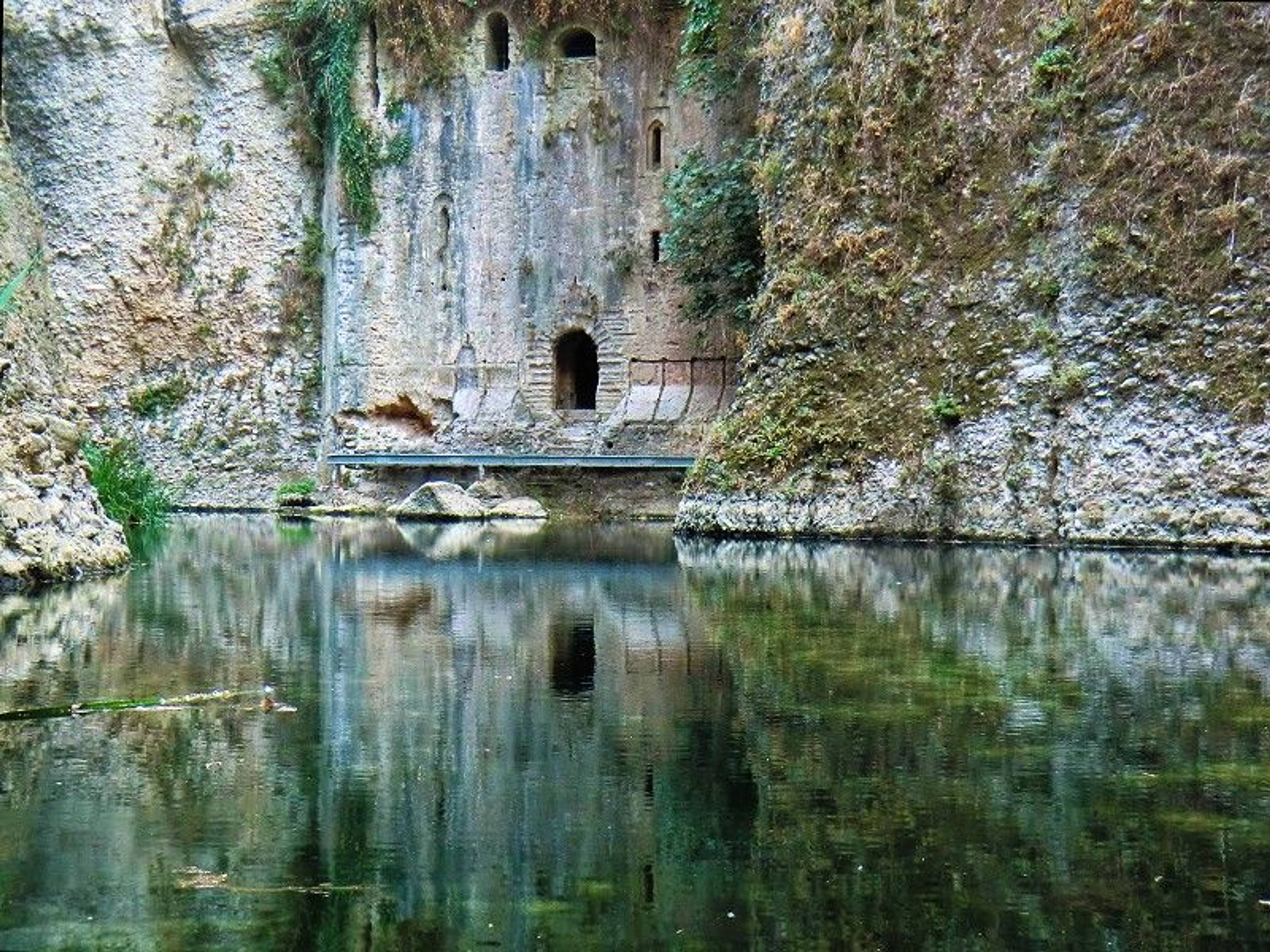 Kamienna ściana mostu w wąwozie, w której są otwory pozwalające wyjść na zewnątrz, do rzeki, która znajduje się na pierwszym planie zdjęcia. 
