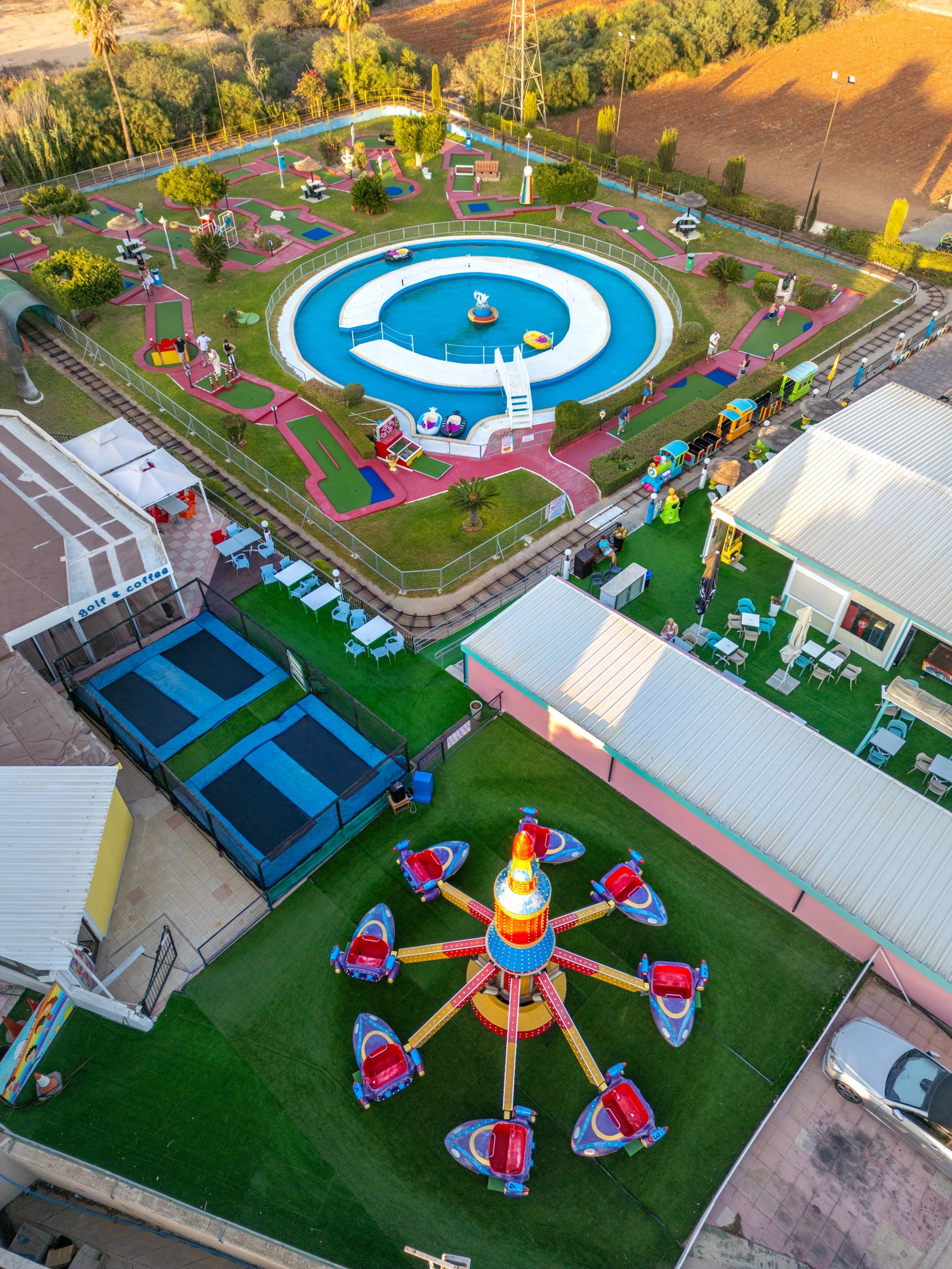 Widok z lotu ptaka na park rozrywki Star Leisure Mini Golf na Cyprze z kolorowymi atrakcjami, trampolinami i torami mini golfa. W centrum znajduje się okrągły basen z wodnymi zabawkami.