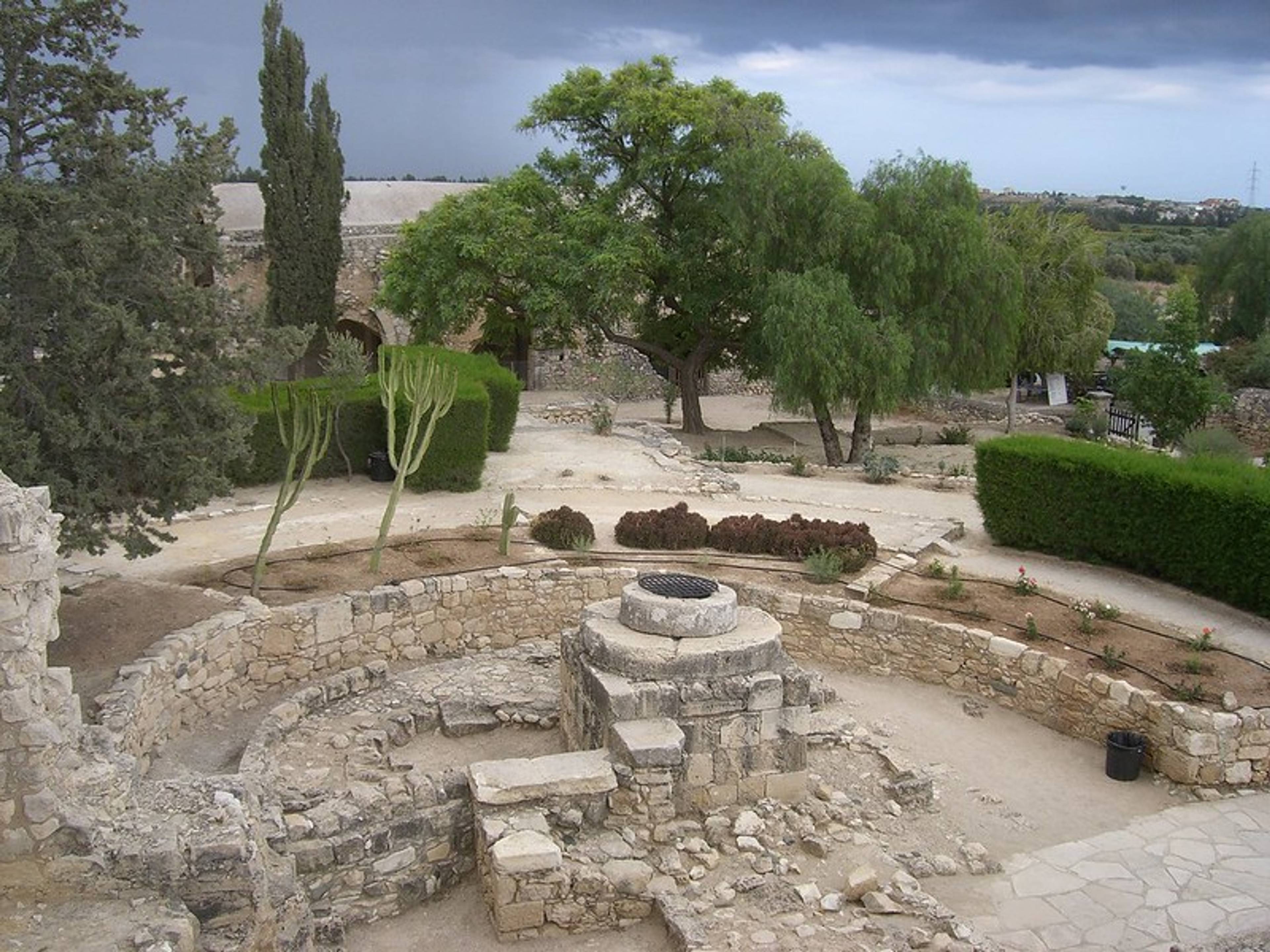 Stanowisko archeologiczne z kamiennymi ruinami i drzewami w tle.