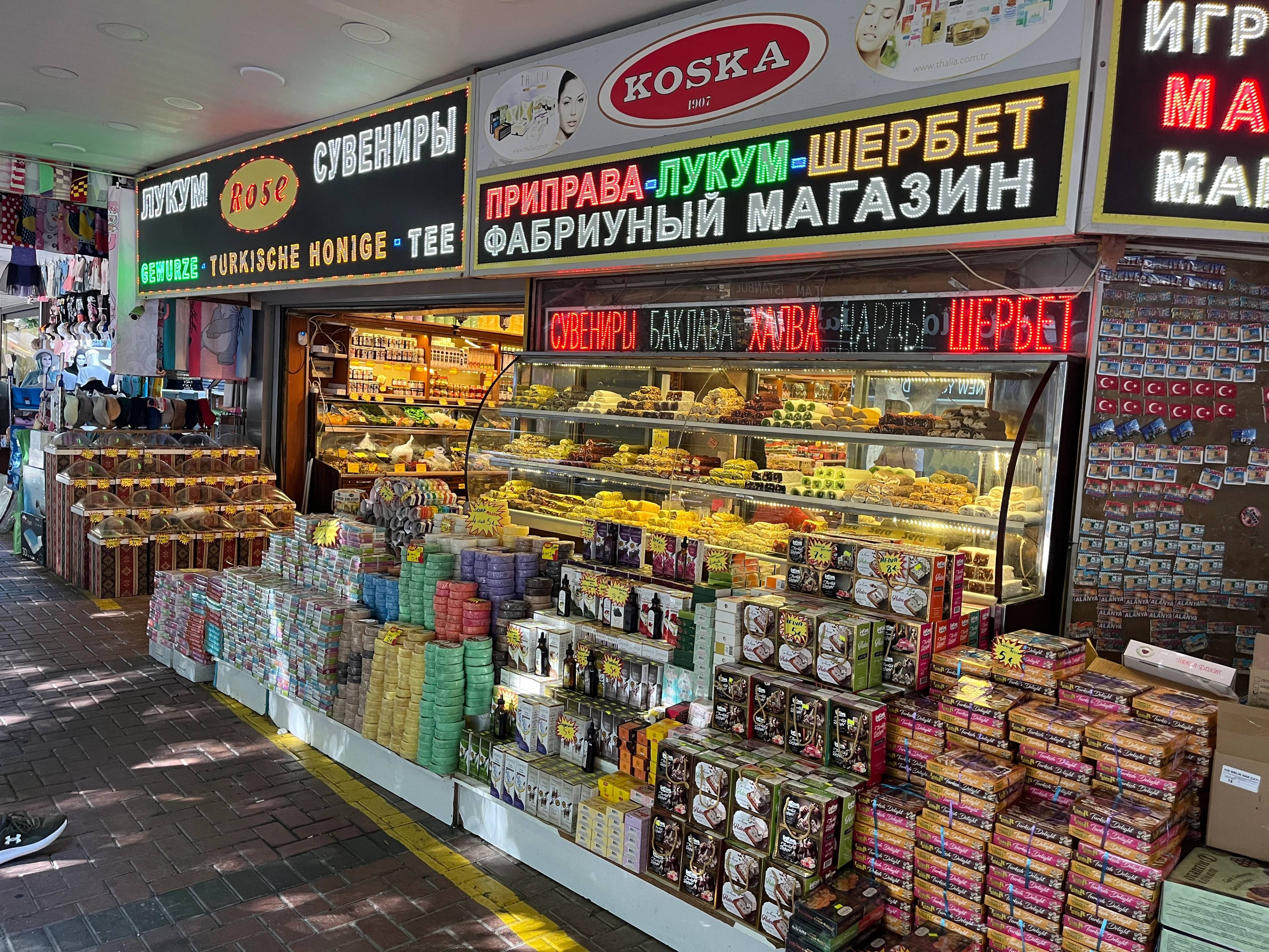 Stoisko z różnorodnymi słodyczami i produktami spożywczymi, z szyldami w języku rosyjskim i tureckim.