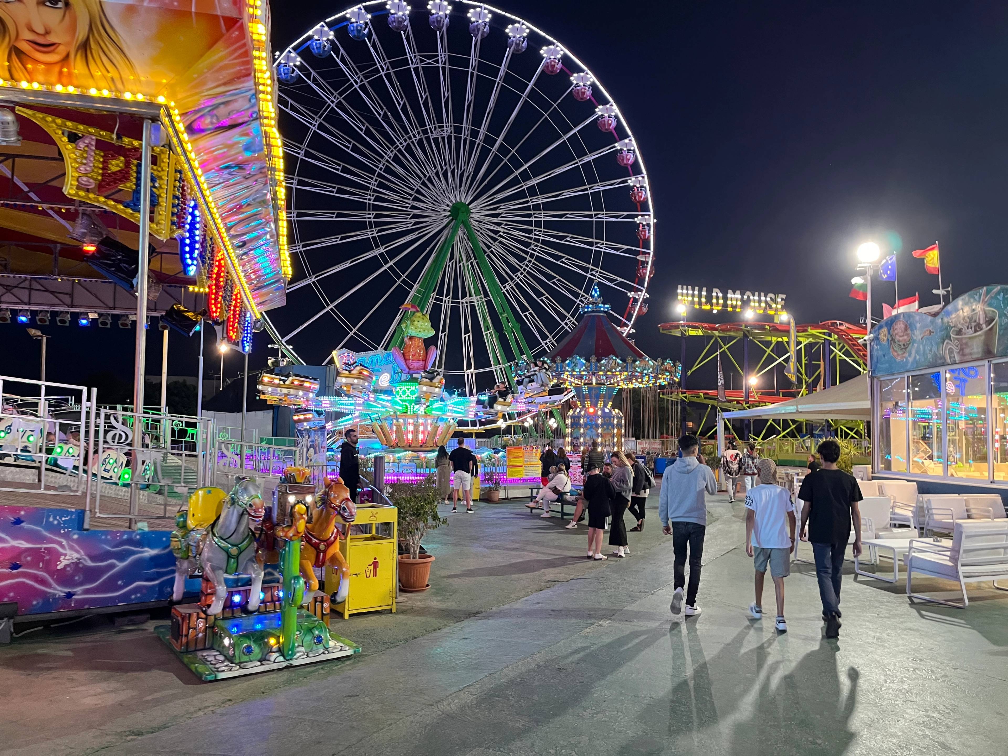 Oświetlone wesołe miasteczko w Ayia Napa na Cyprze z dużym diabelskim młynem, karuzelami i kolorowymi atrakcjami.