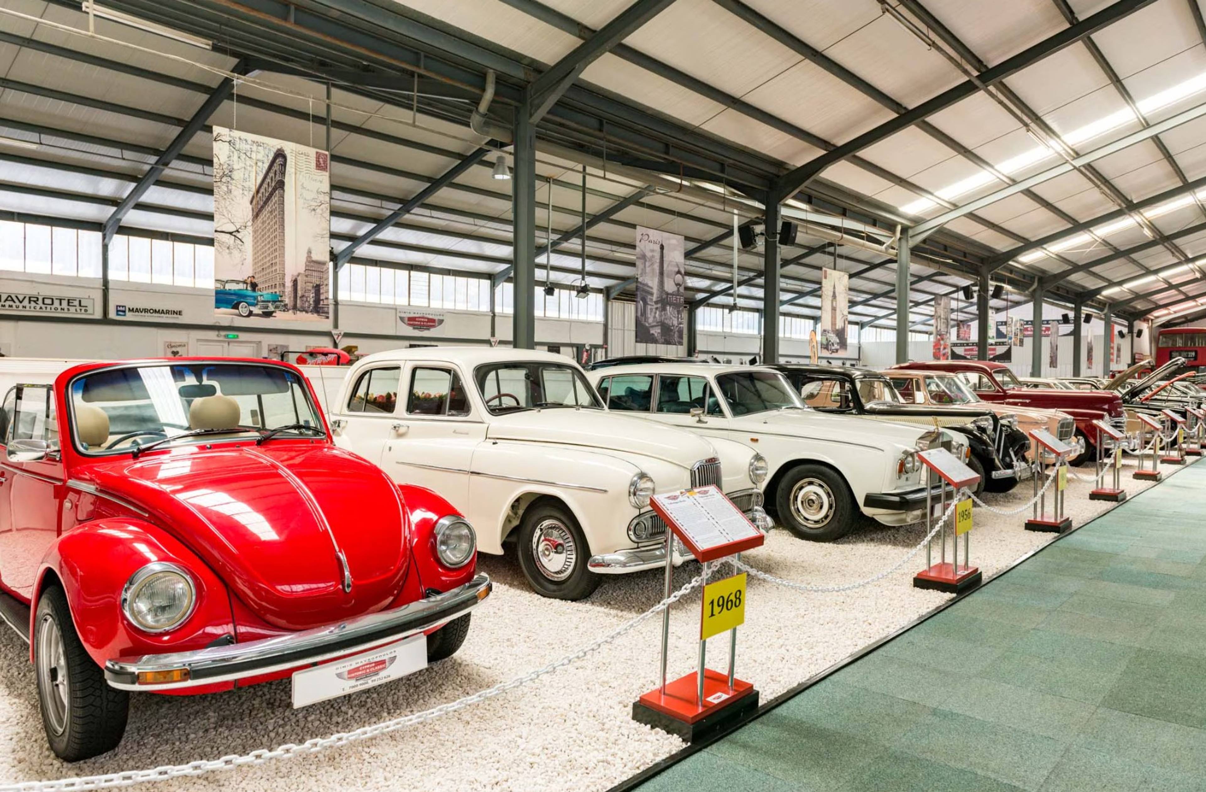 Wystawa zabytkowych samochodów w hali, na pierwszym planie czerwony Volkswagen Garbus, dalej inne klasyczne modele.