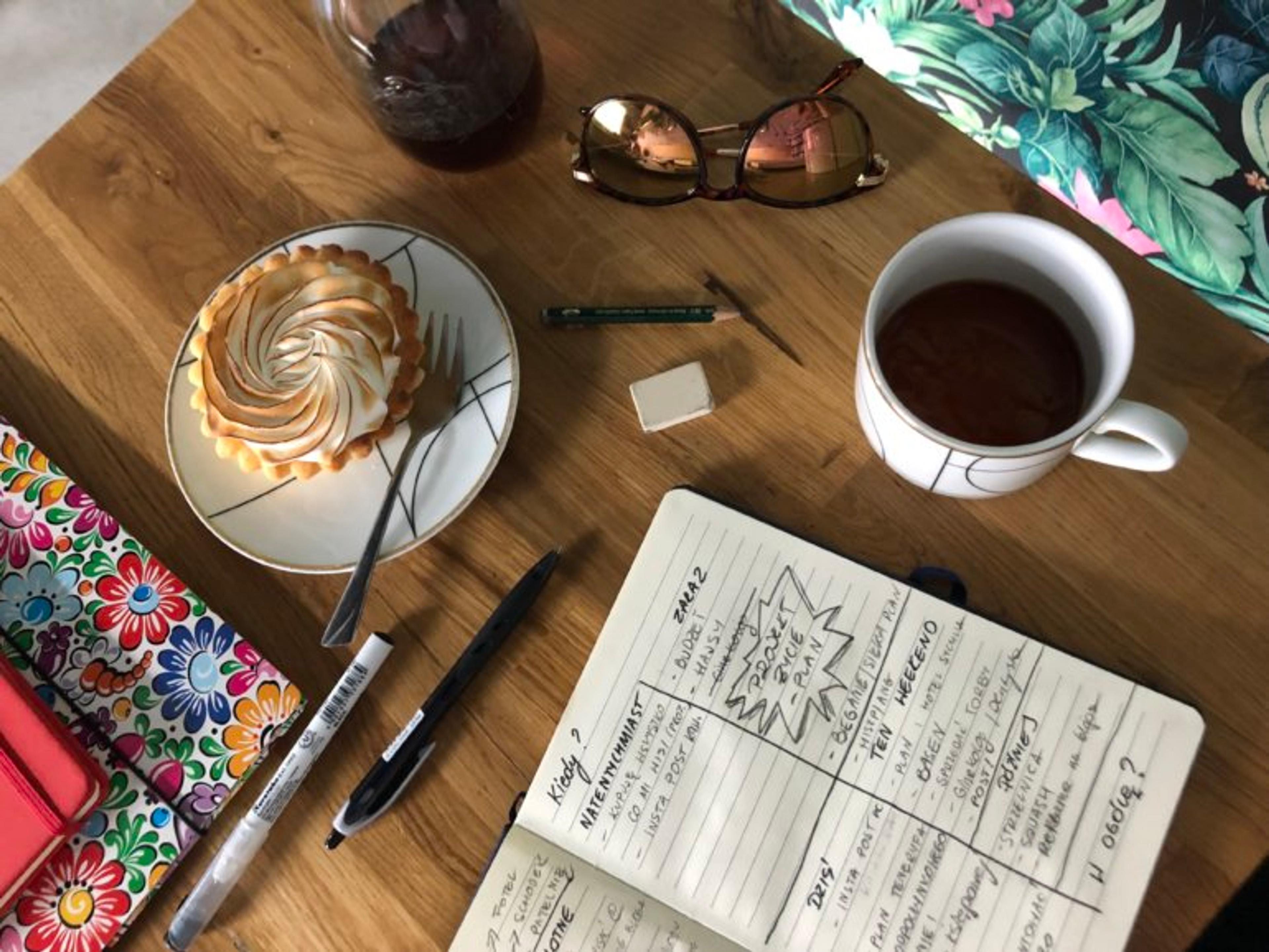 Notes, kawa, ciastko, teczka i długopisy na stole w kawiarni