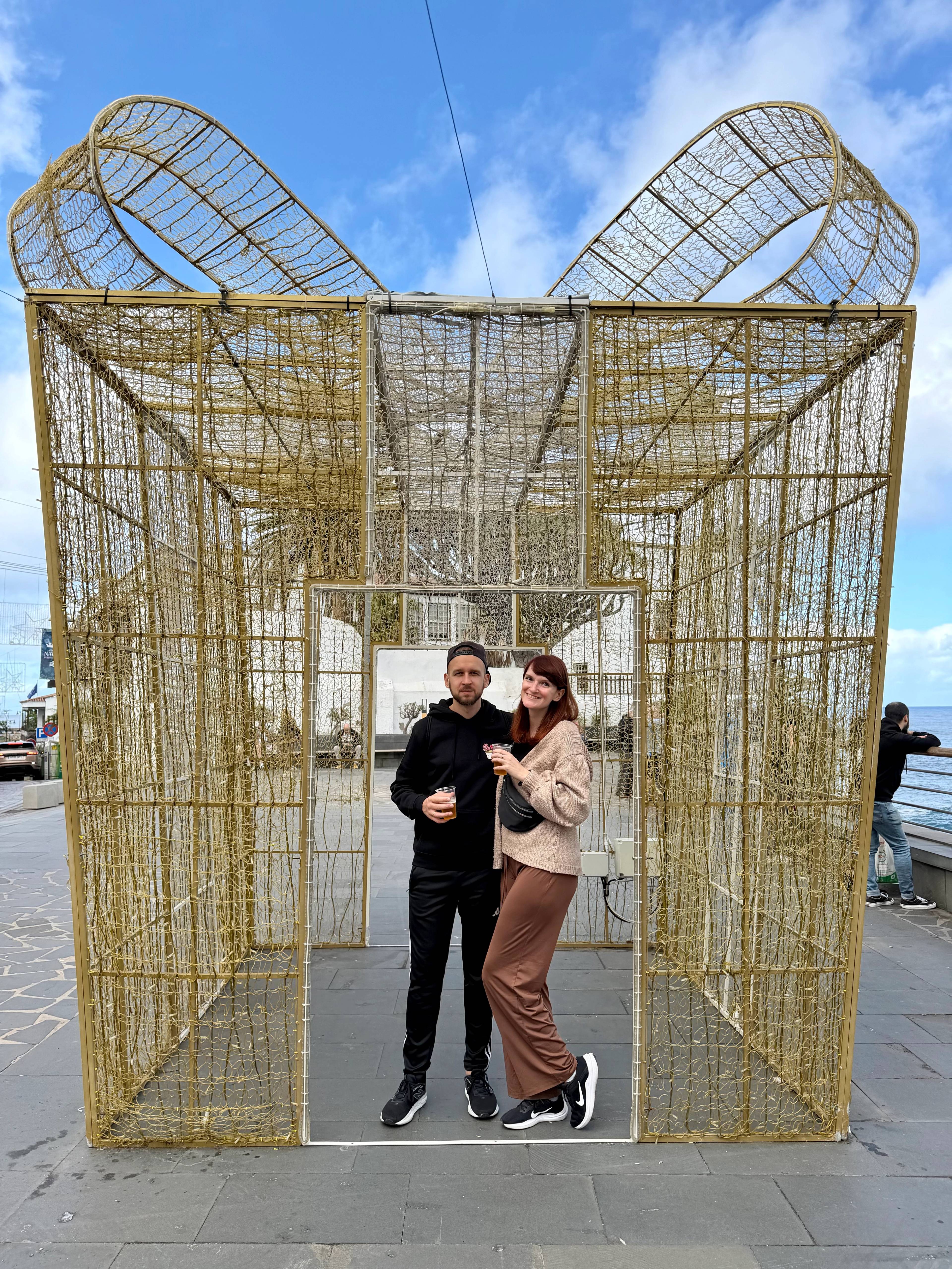 Para stoi w złotej, dekoracyjnej konstrukcji w kształcie prezentu świątecznego.