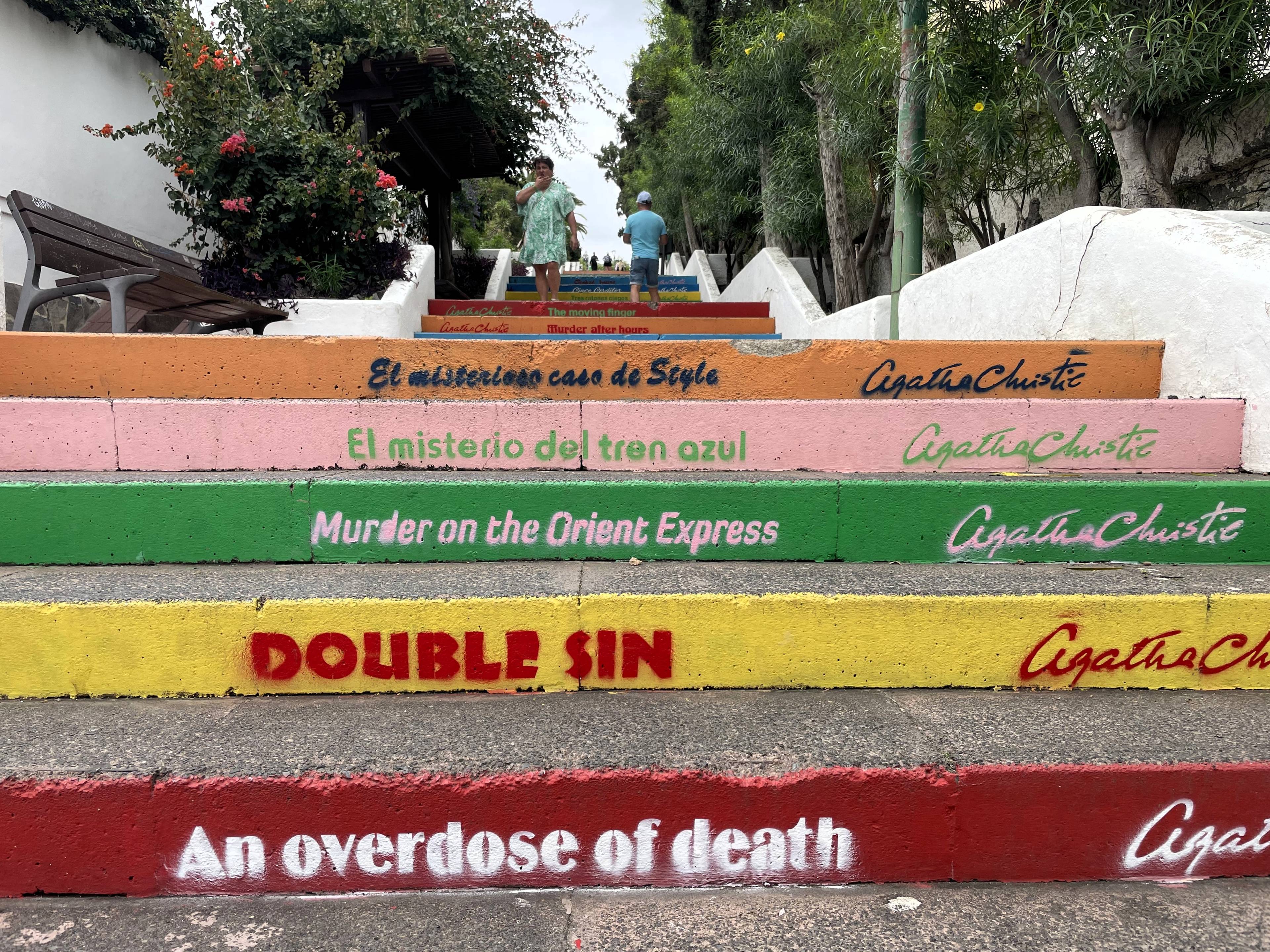 Kolorowe schody z napisami - tytułami książek Agaty Christie, w otoczeniu białych murów i roślinności.