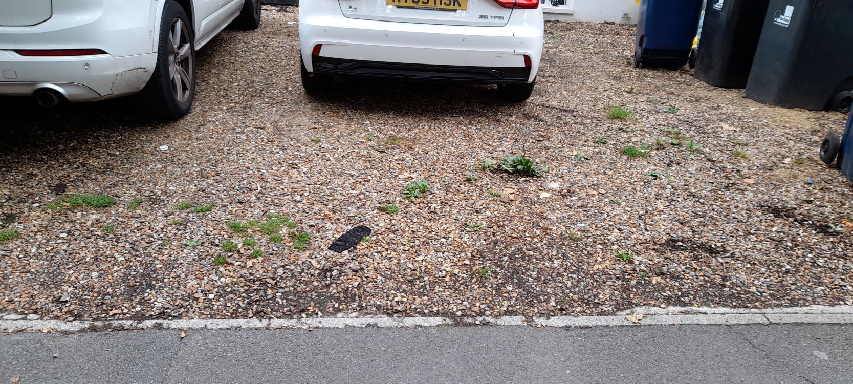 cars parked on gravel surface in a front garden with weeds growing