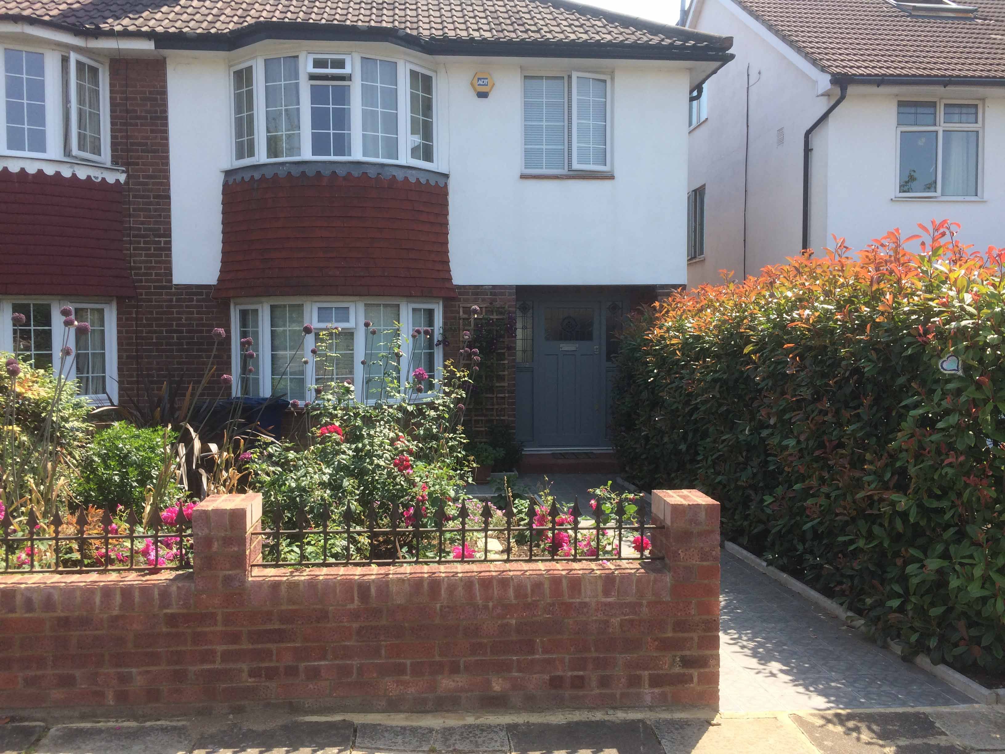 a front garden with flowers, a wall and a path to the door