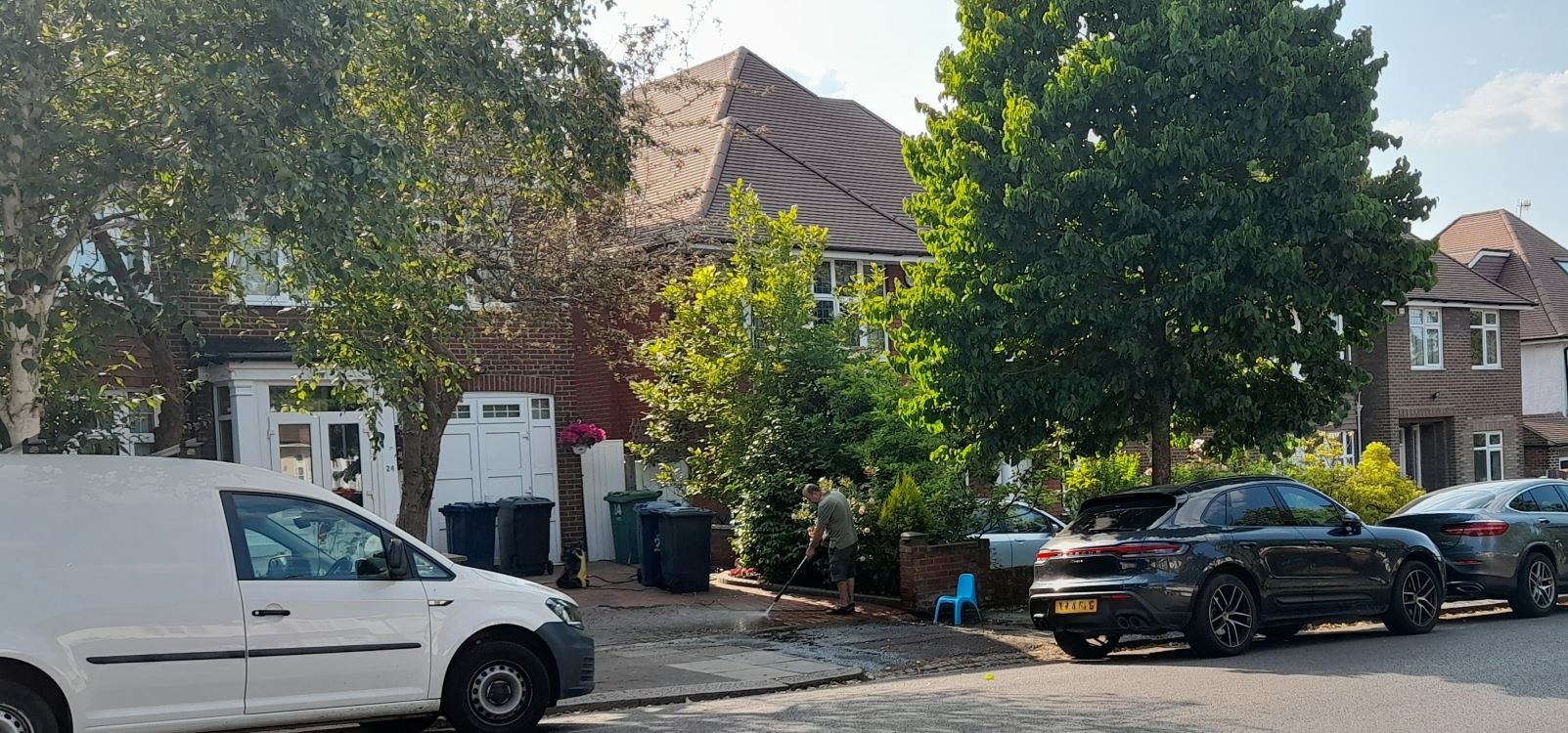 A person pressure-washing a front garden with a hose.