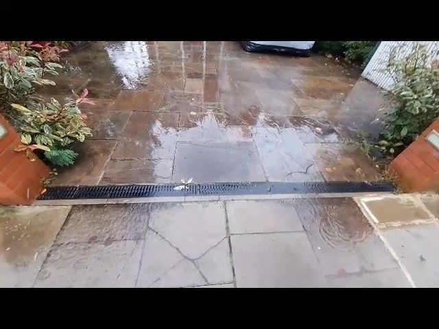 a paved front garden and rain running over the top of a drainage grille