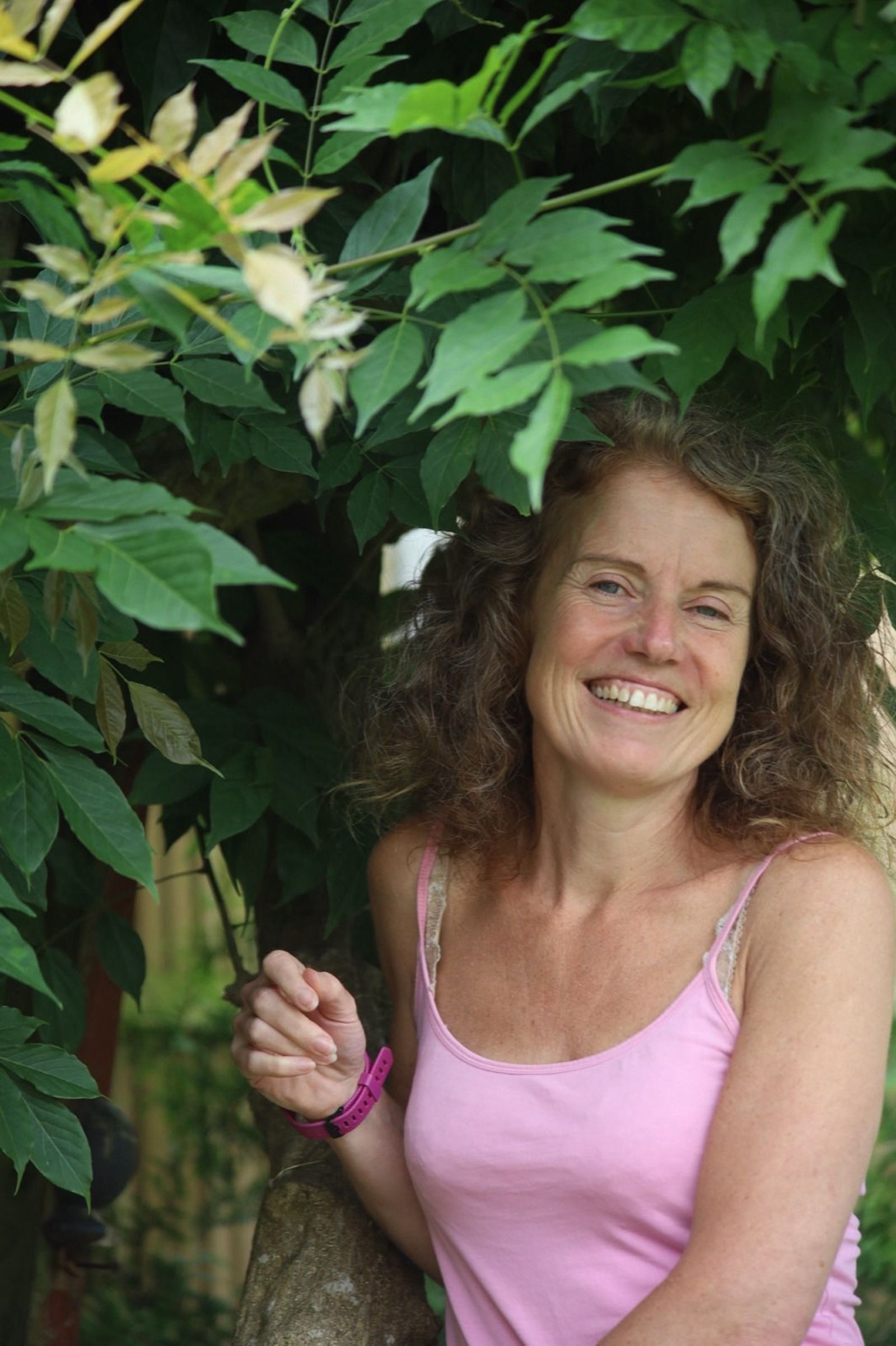 Gina smiling among green leaves