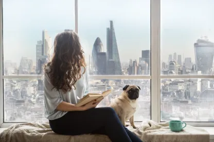 Woman reading beside a dog with the City of London skyline beyond the window