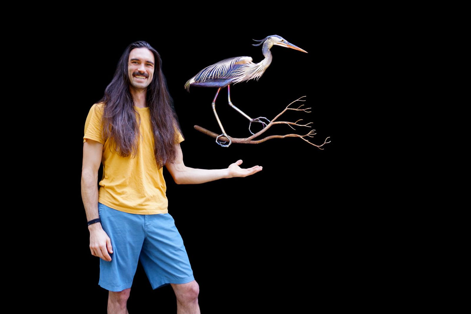 Metal sculptor Aiden Dale beside his life-sized stainless steel blue heron sculpture, handmade and flame-painted without paint or enamel.