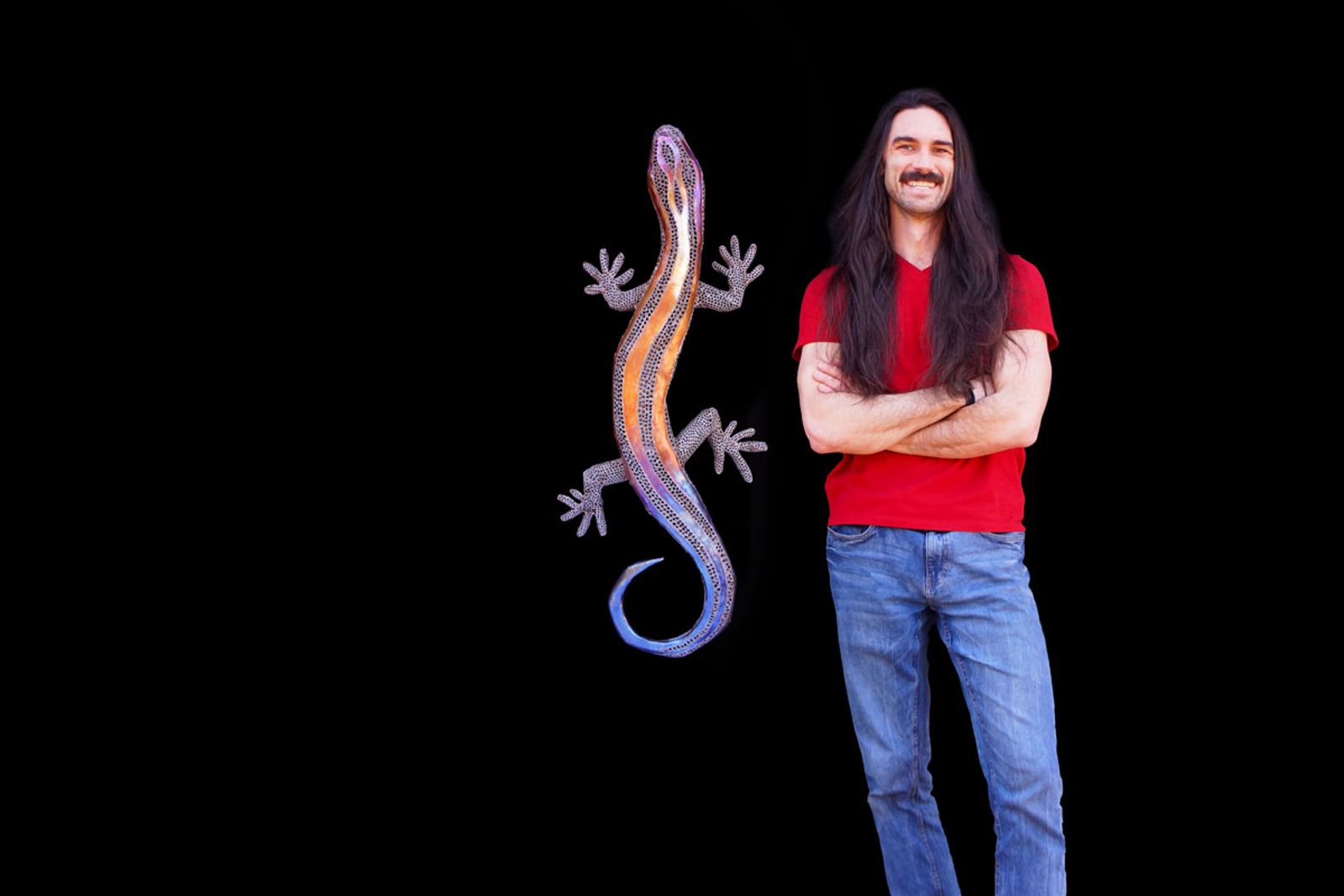 Artist Aiden Dale beside his stainless steel blue-tailed skink sculpture, handmade with intricate grinder and torch detailing.