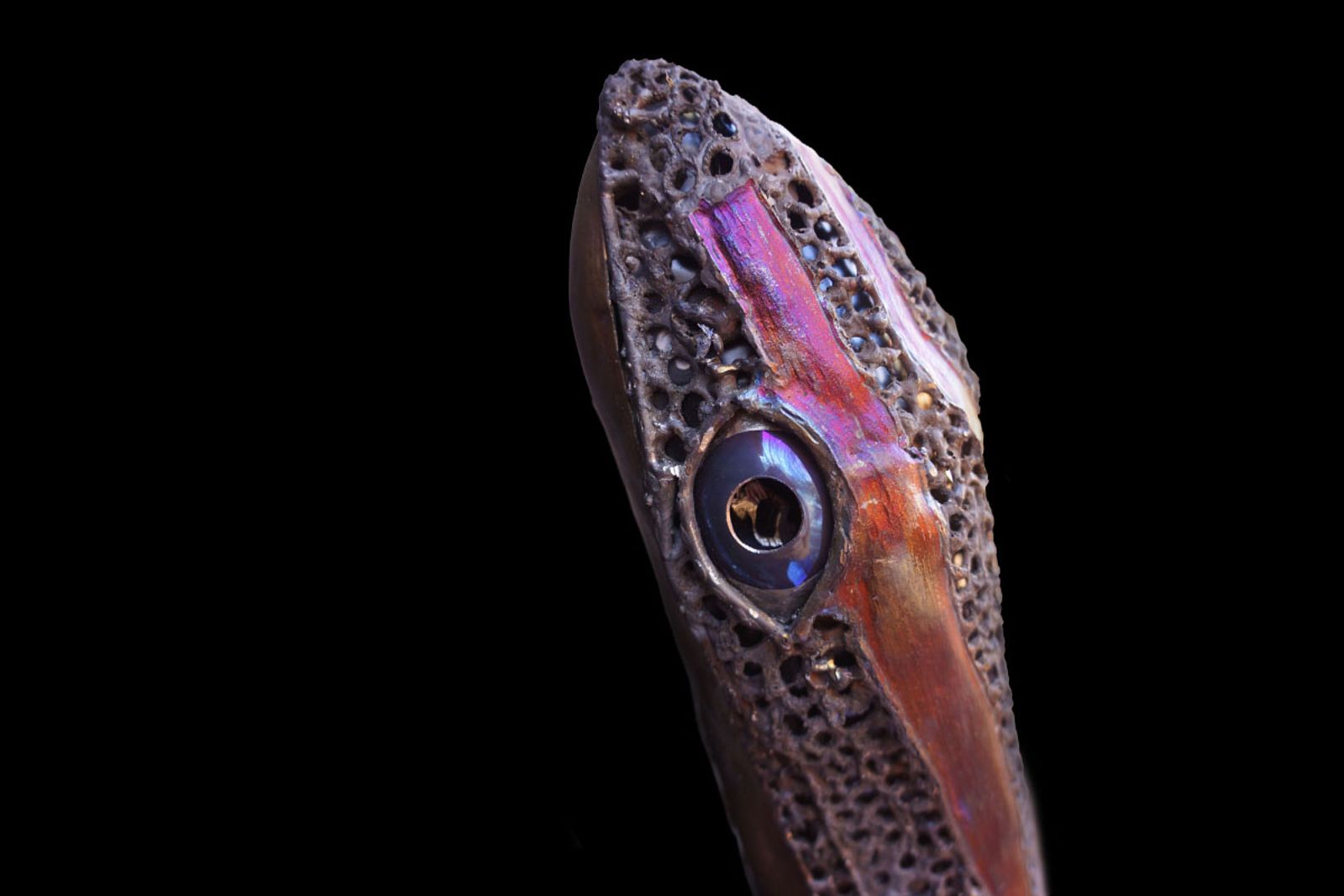 Close-up of polished mirror-finish skink eye in stainless steel with hand-cut pupil and painted black center for lifelike depth.