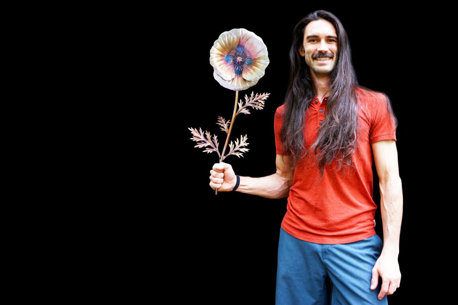 Artist Aiden Dale holding his stainless steel white poppy sculpture, handmade with torch patina and detailed stamen bundle.