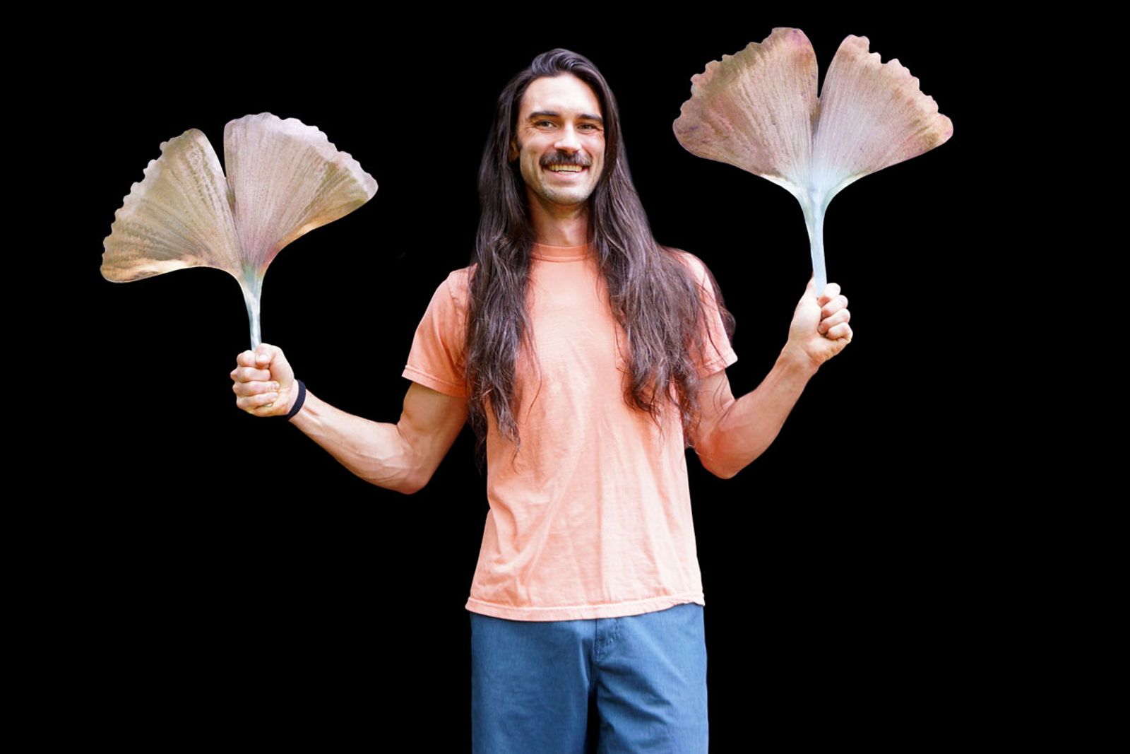 Artist Aiden Dale holding two large stainless steel ginkgo leaf sculptures, each hand-shaped and flame-painted.