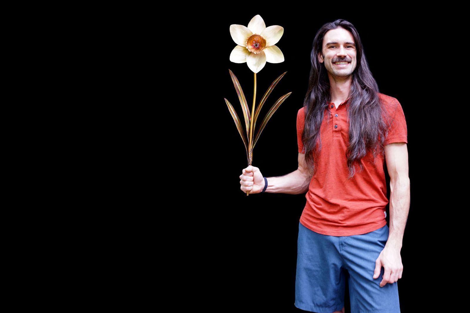 Metal sculptor Aiden Dale holding his stainless steel daffodil with white petals and gold center, crafted entirely by torch and grinder
