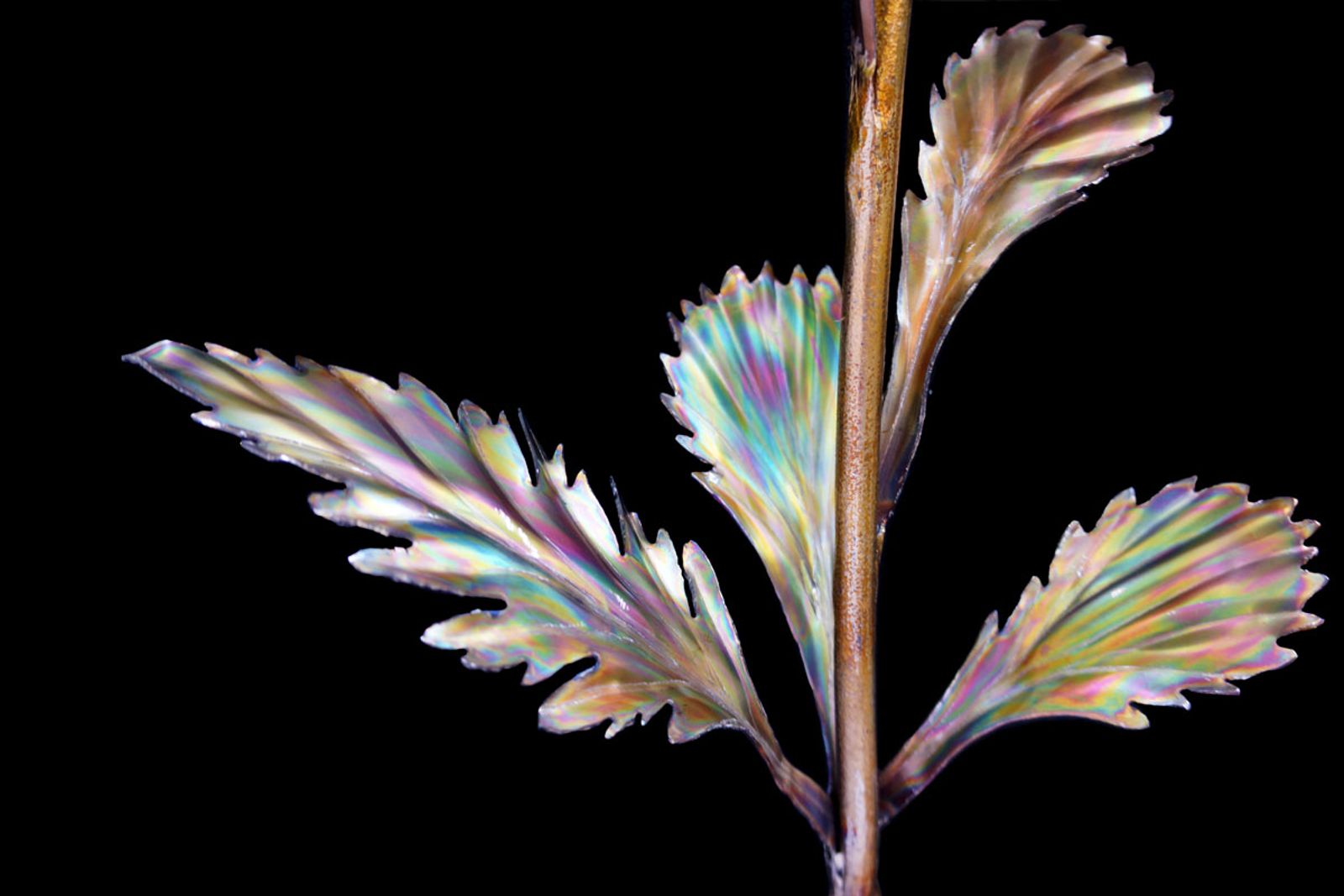 Leaf and stem detail of stainless steel daisy sculpture, flame-colored greens and bead-rolled veins for lifelike texture.