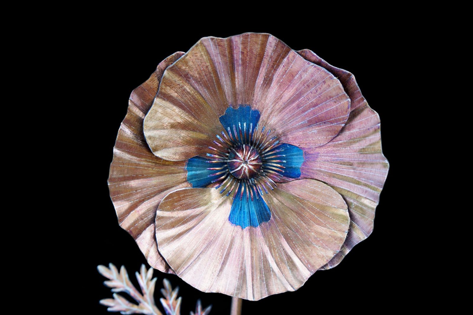 Close-up of golden stainless steel poppy bloom with hand-bent stamens and a glowing blue torch-colored center.
